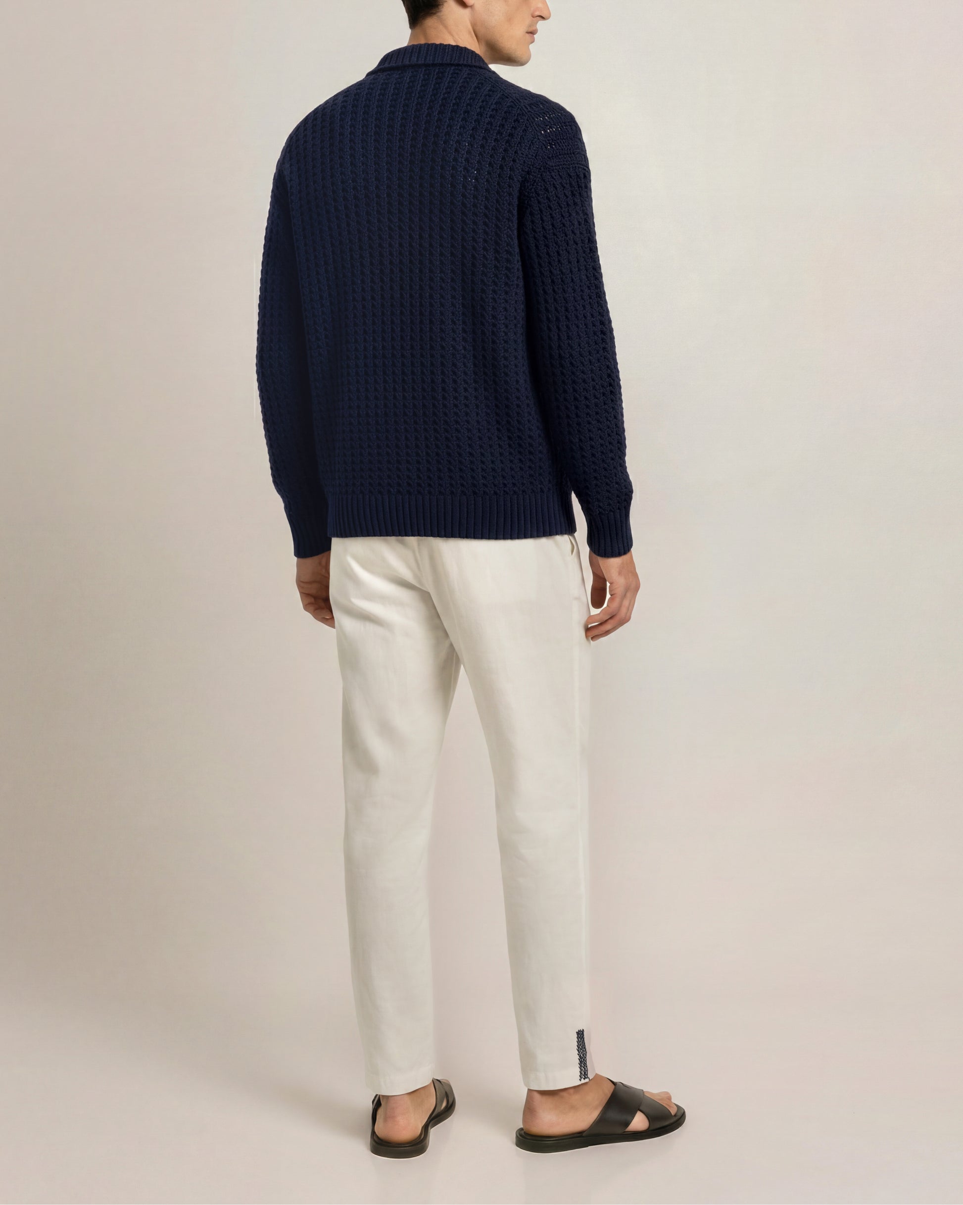 Person wearing a navy sweater and white pants on a plain background