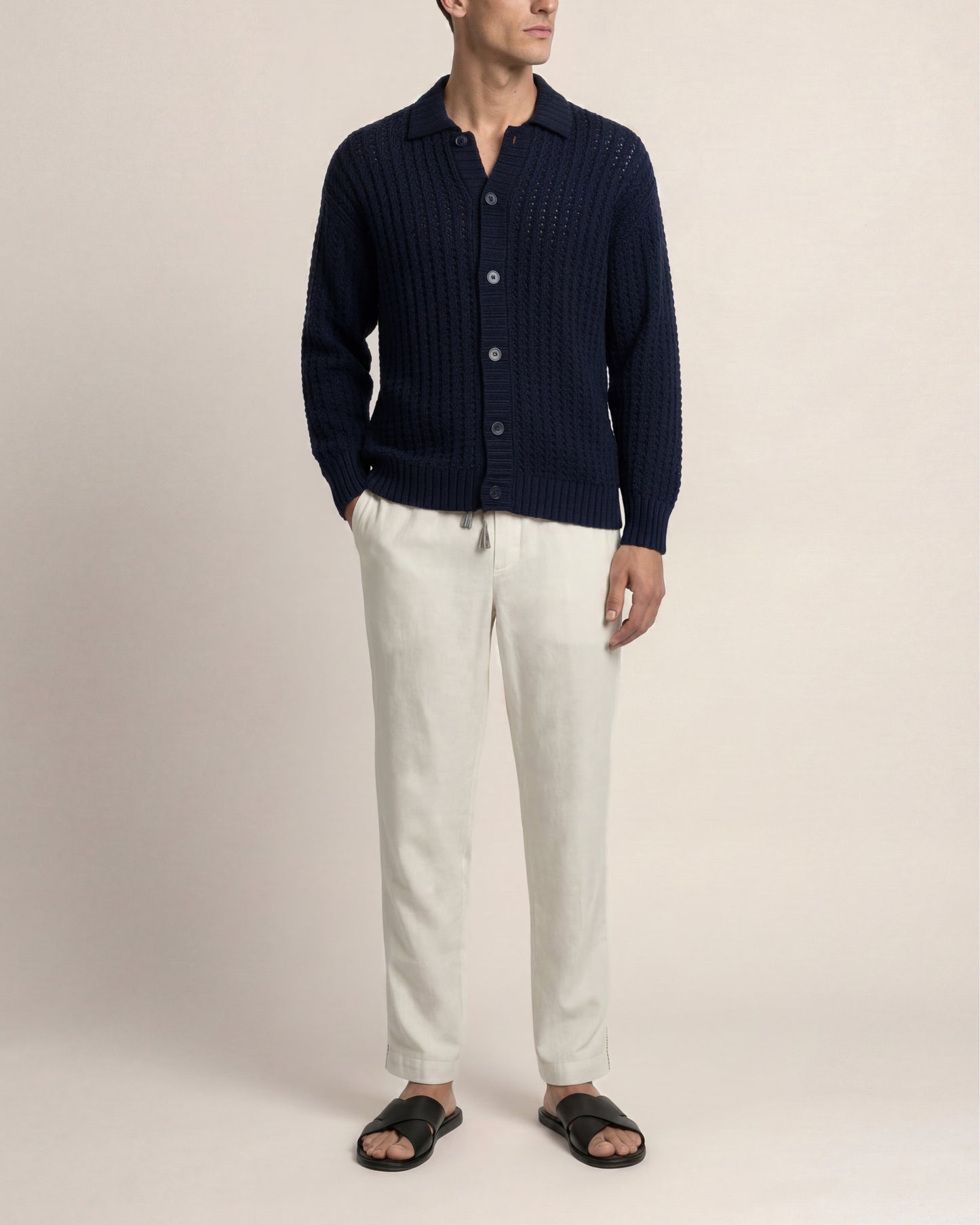 Person wearing a navy blue knitted cardigan and white pants on a beige background