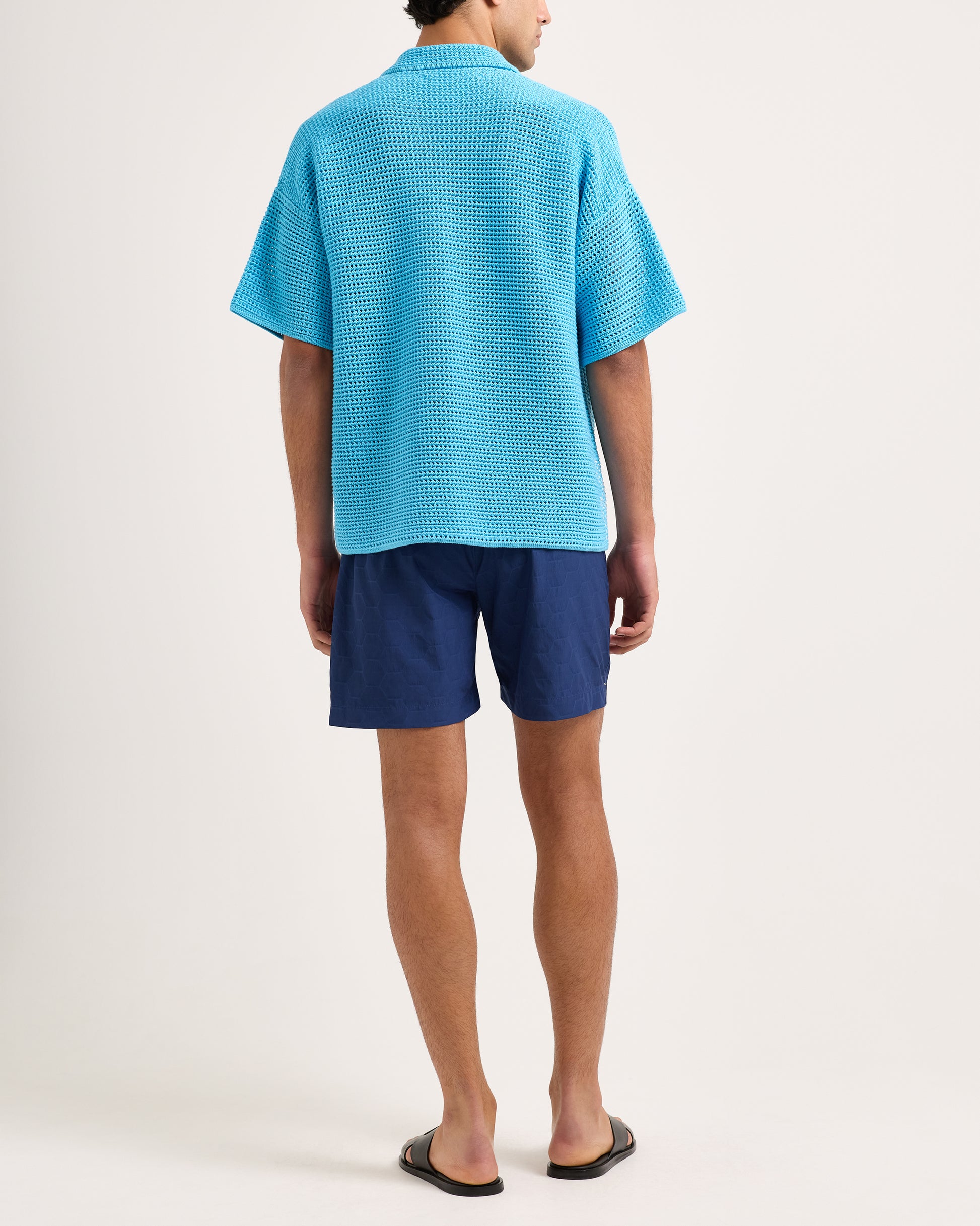 Person wearing a blue textured shirt and navy shorts on a white background