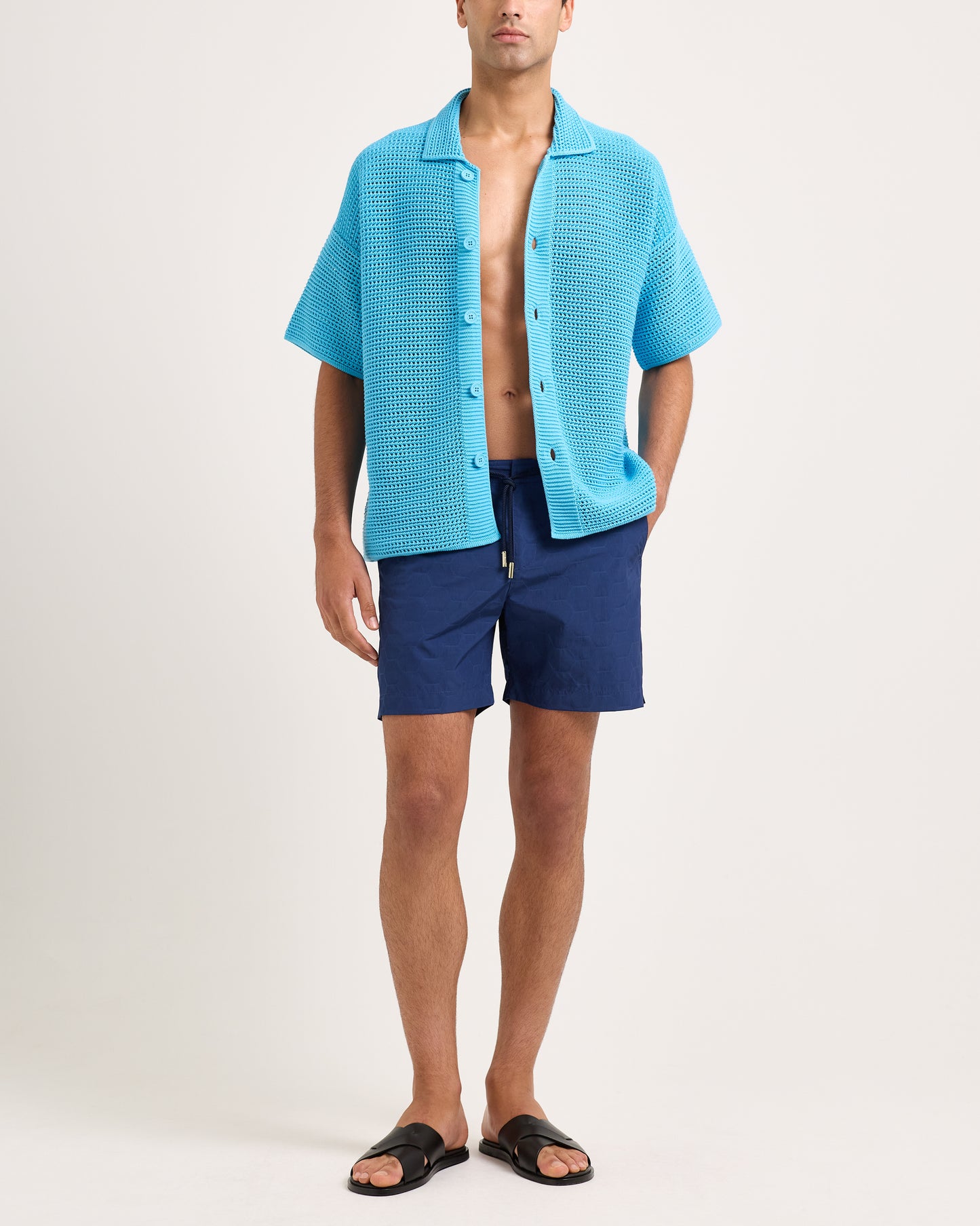 Man wearing a blue textured shirt over a blue swimsuit on a white background