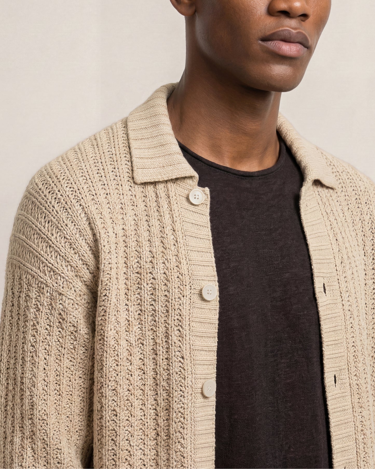 Man wearing a beige knitted cardigan over a dark shirt against a neutral background