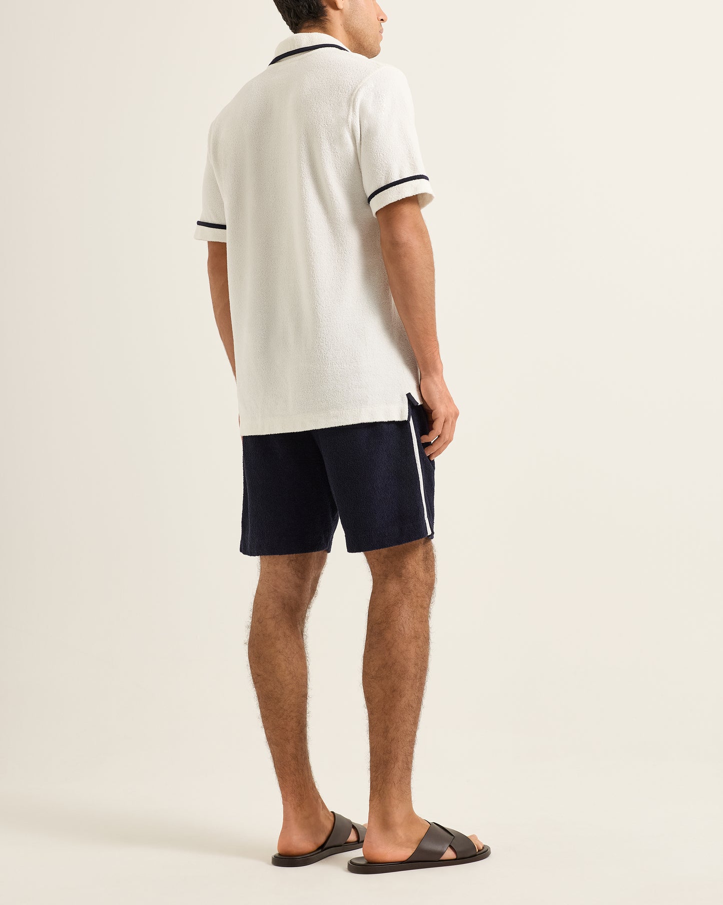 Person wearing a white polo shirt and navy shorts on a plain background