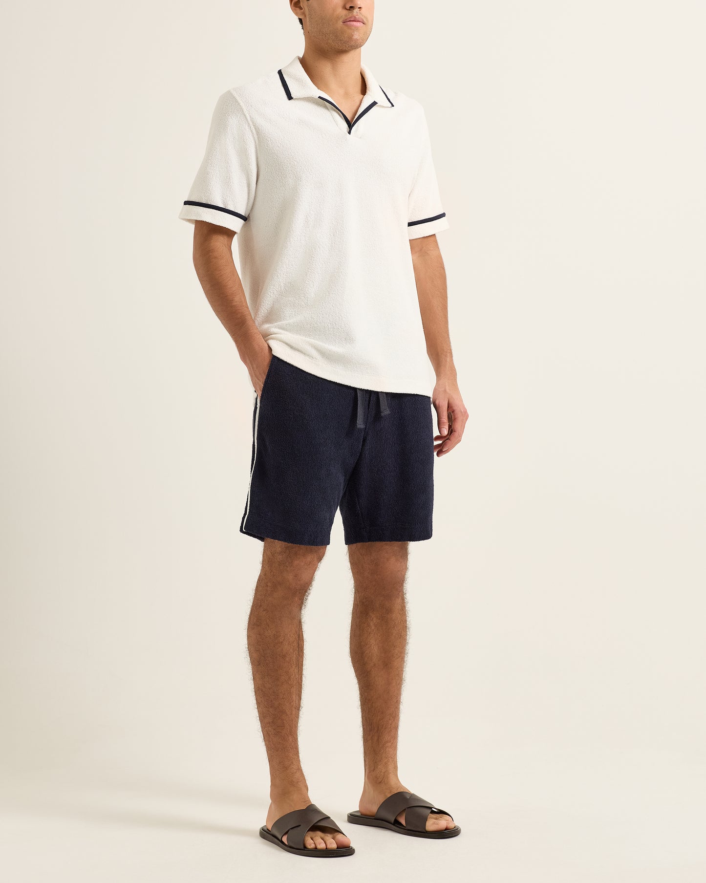 Man wearing a white polo shirt and navy shorts on a beige background