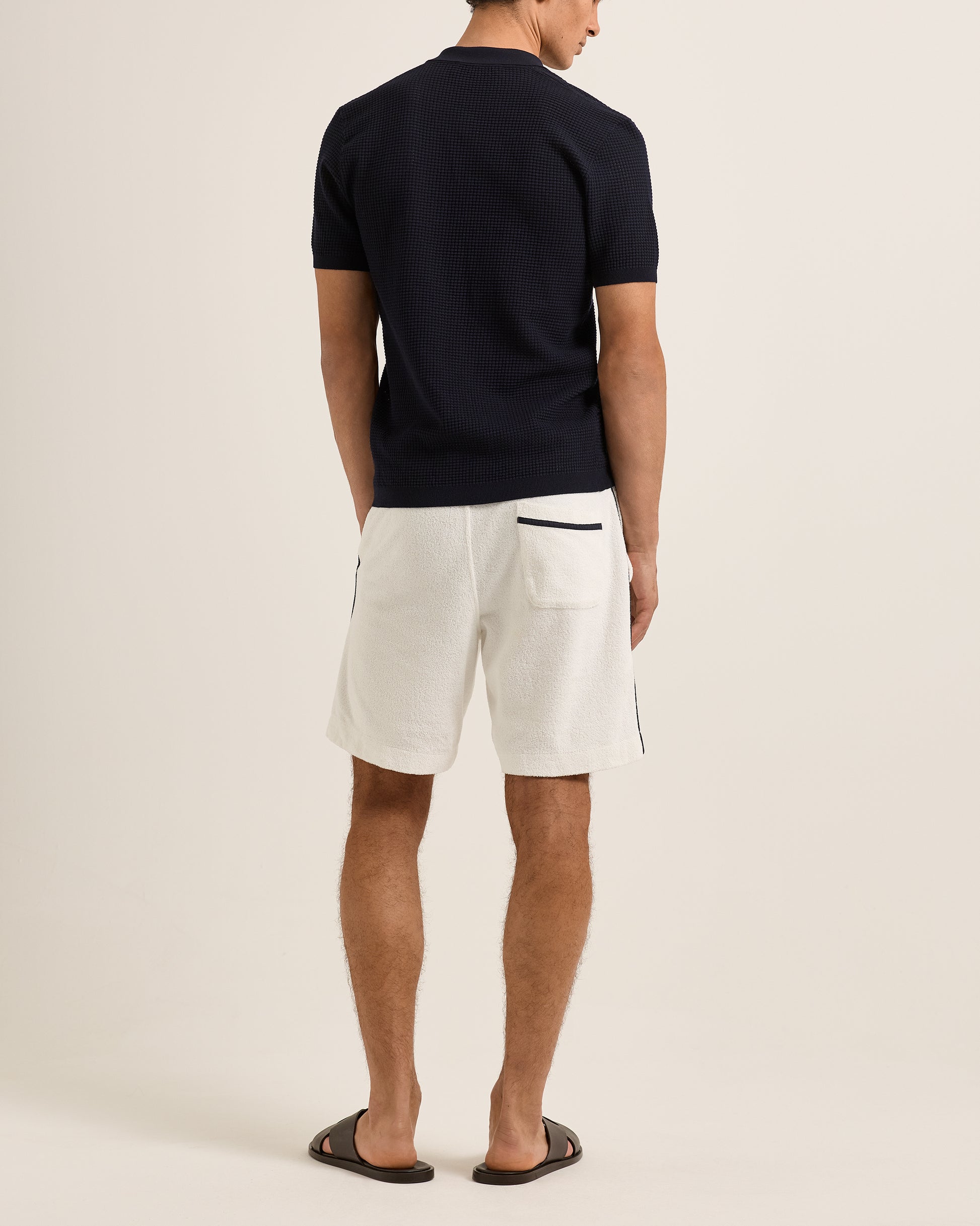 Person wearing a navy polo shirt and white shorts on a beige background