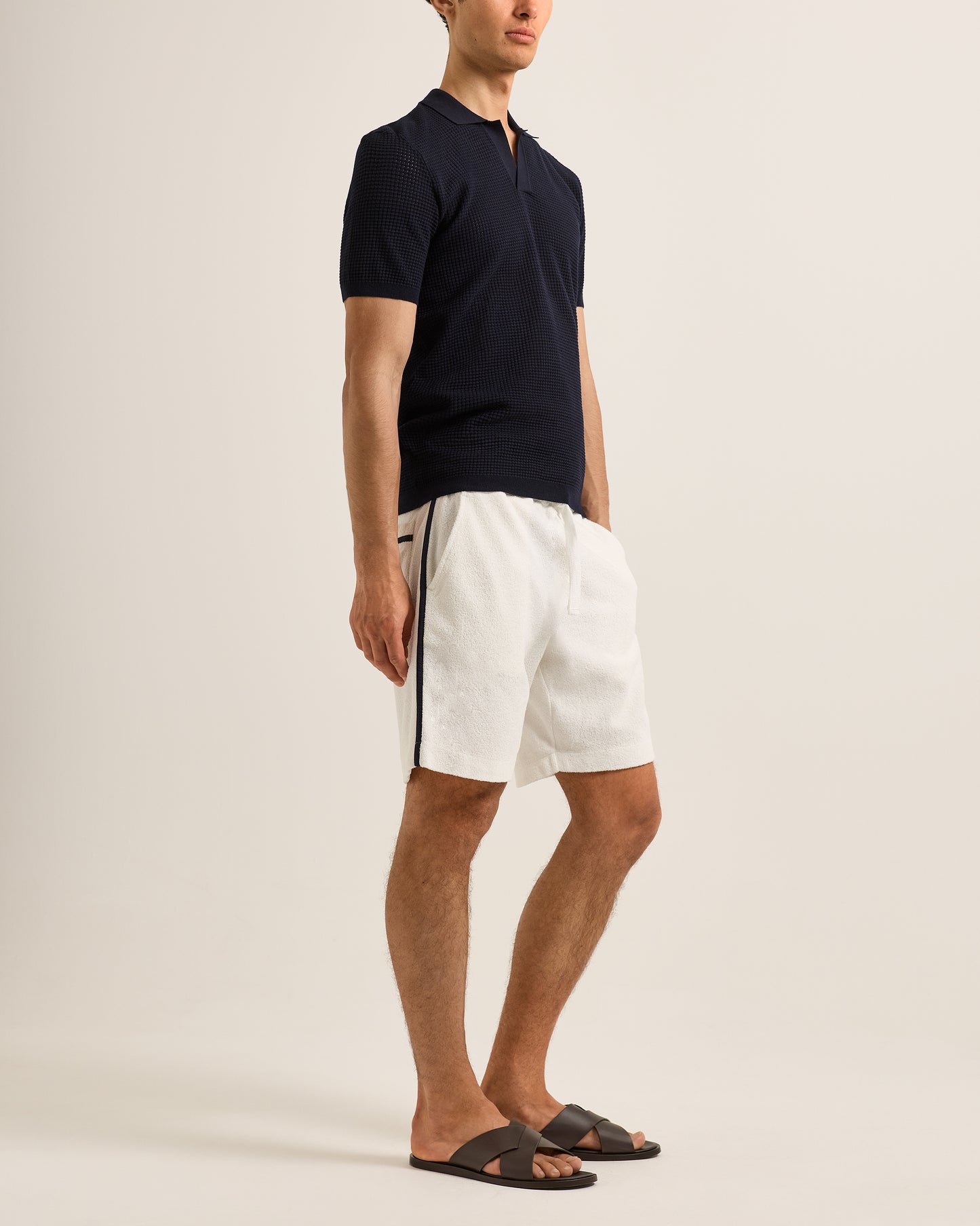 Man wearing a navy polo shirt and white shorts on a beige background