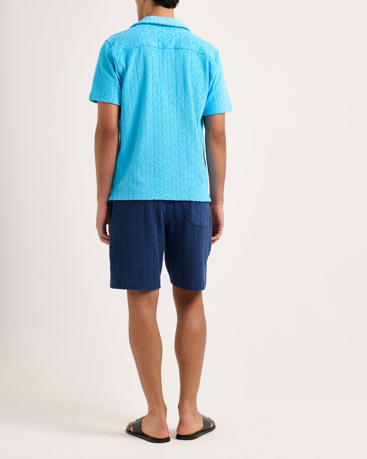 Person wearing a blue patterned shirt and shorts on a white background