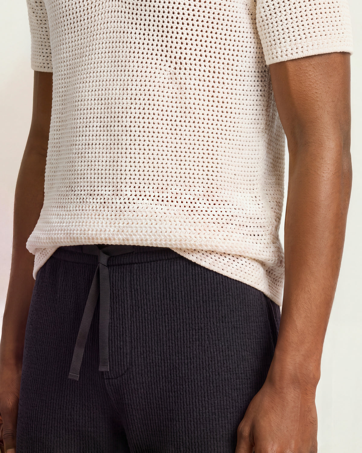 Closeup of navy towelling shorts and white crochet stitch polo shirt on a plain background