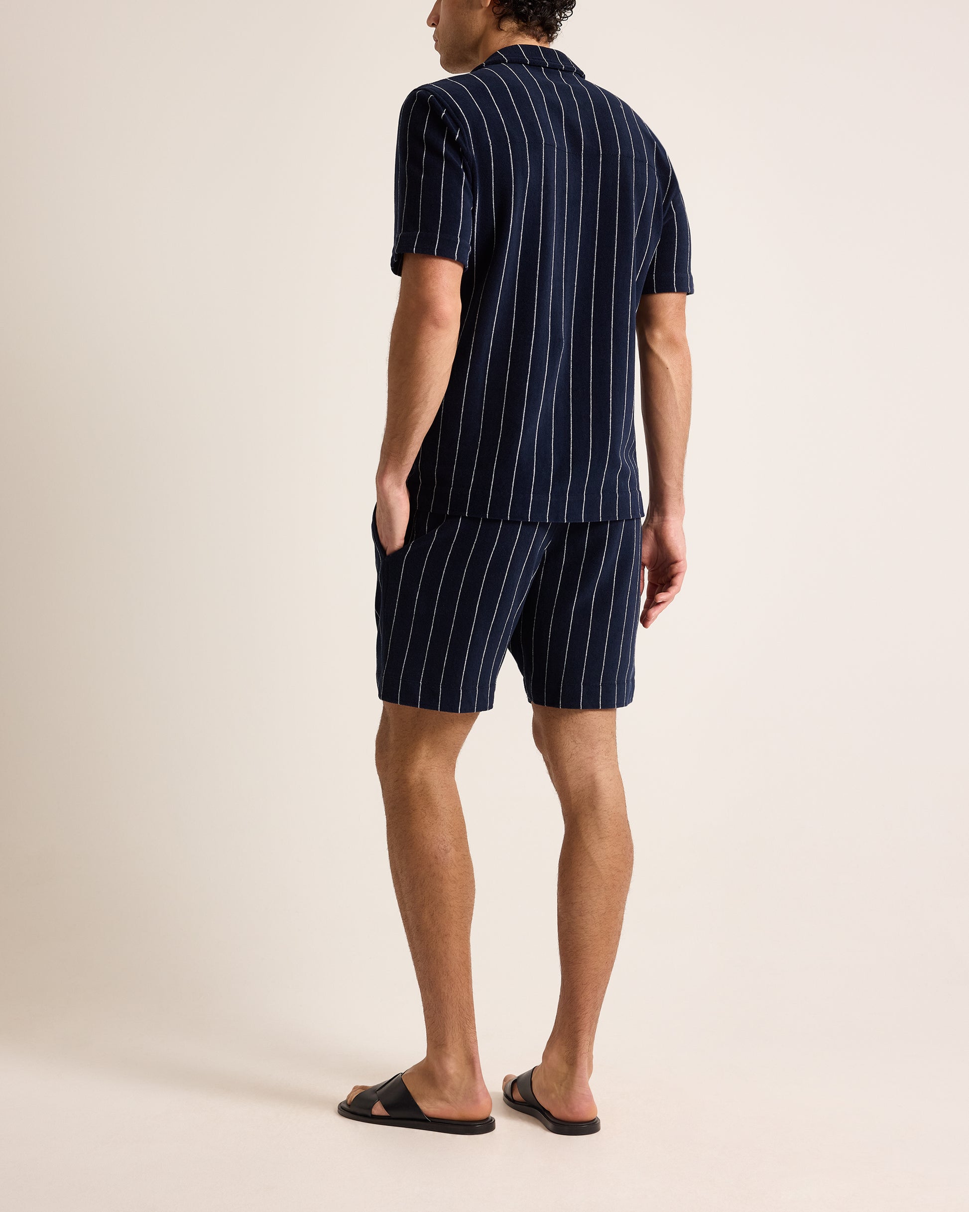 Man wearing a navy pinstripe shirt and shorts set on a beige background