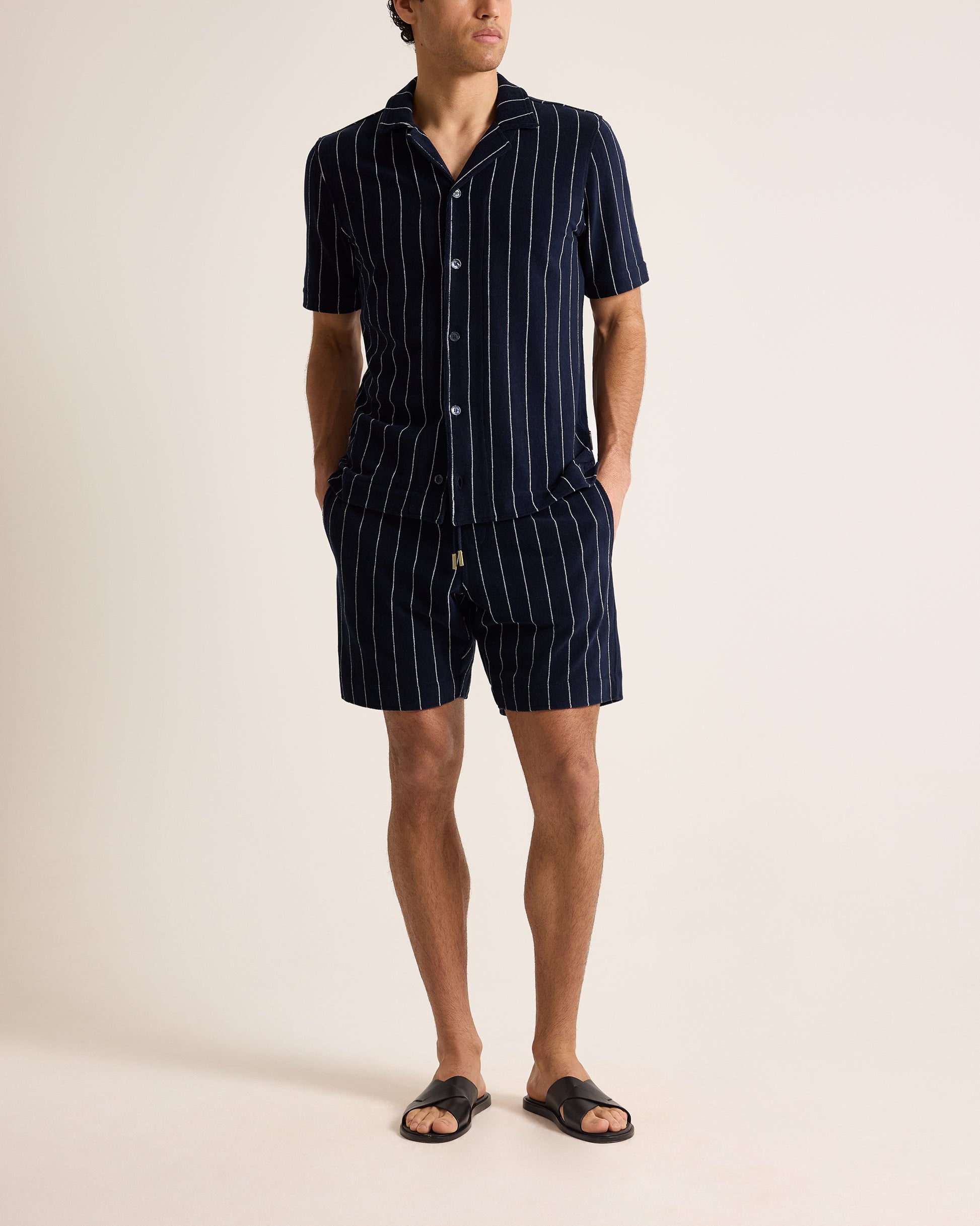 Person wearing a navy pinstripe shirt and shorts set on a beige background