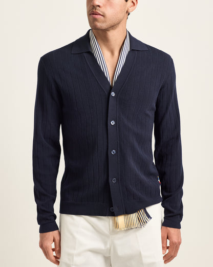 Man wearing a navy cardigan over a striped shirt with a beige background