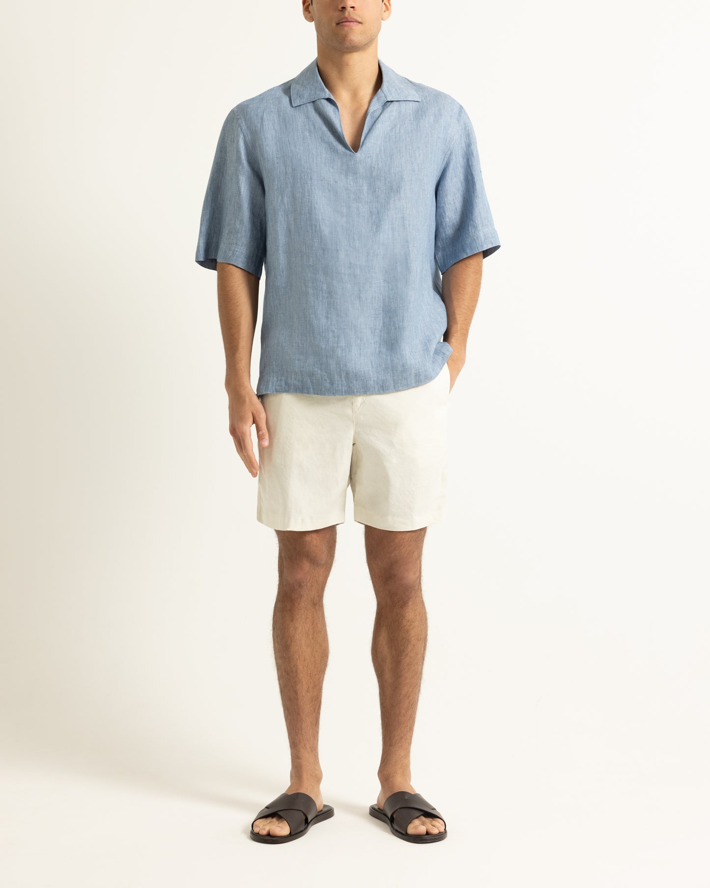 Man wearing a blue short-sleeve shirt and white shorts on a white background