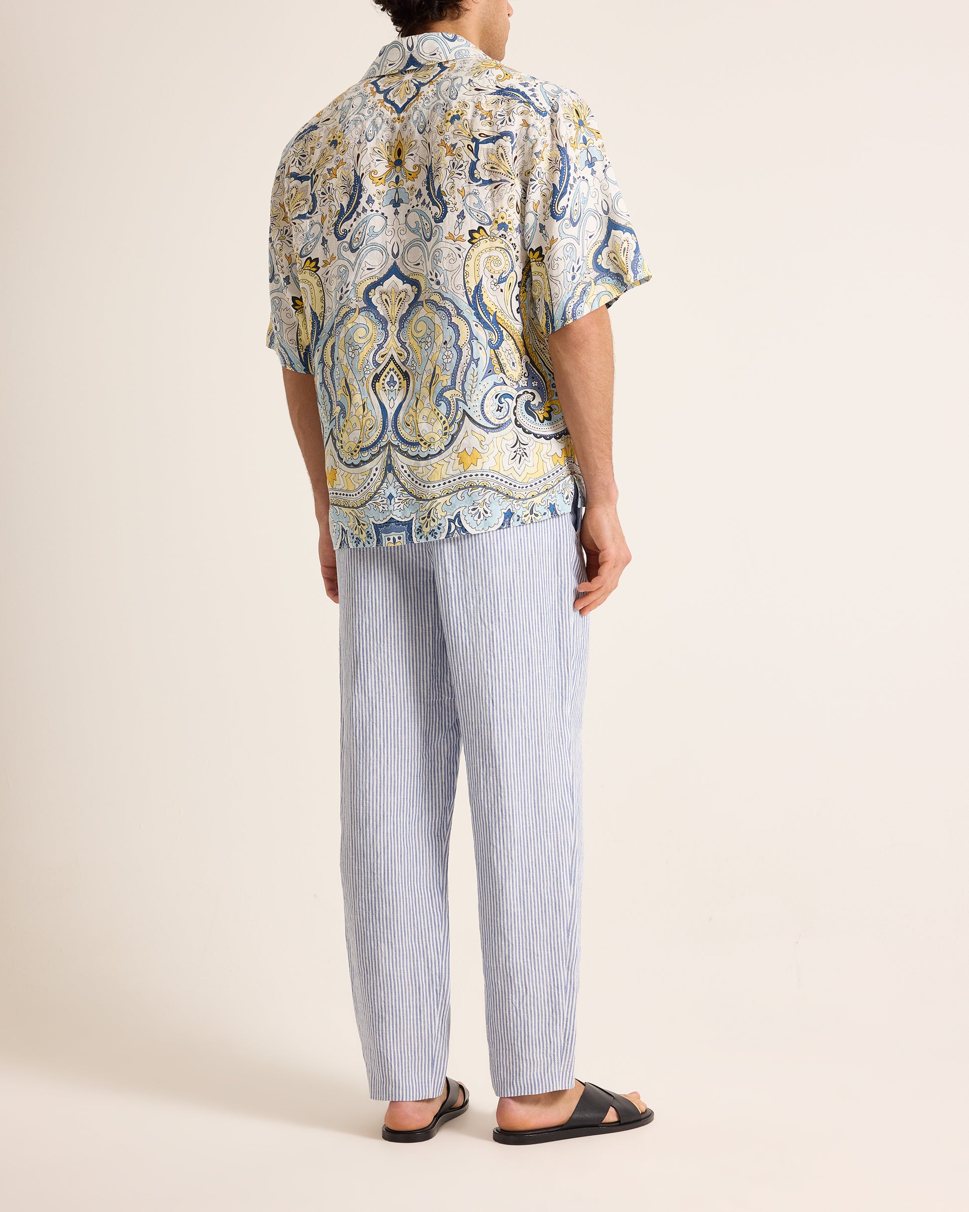 Person wearing a patterned shirt and light blue pants on a beige background