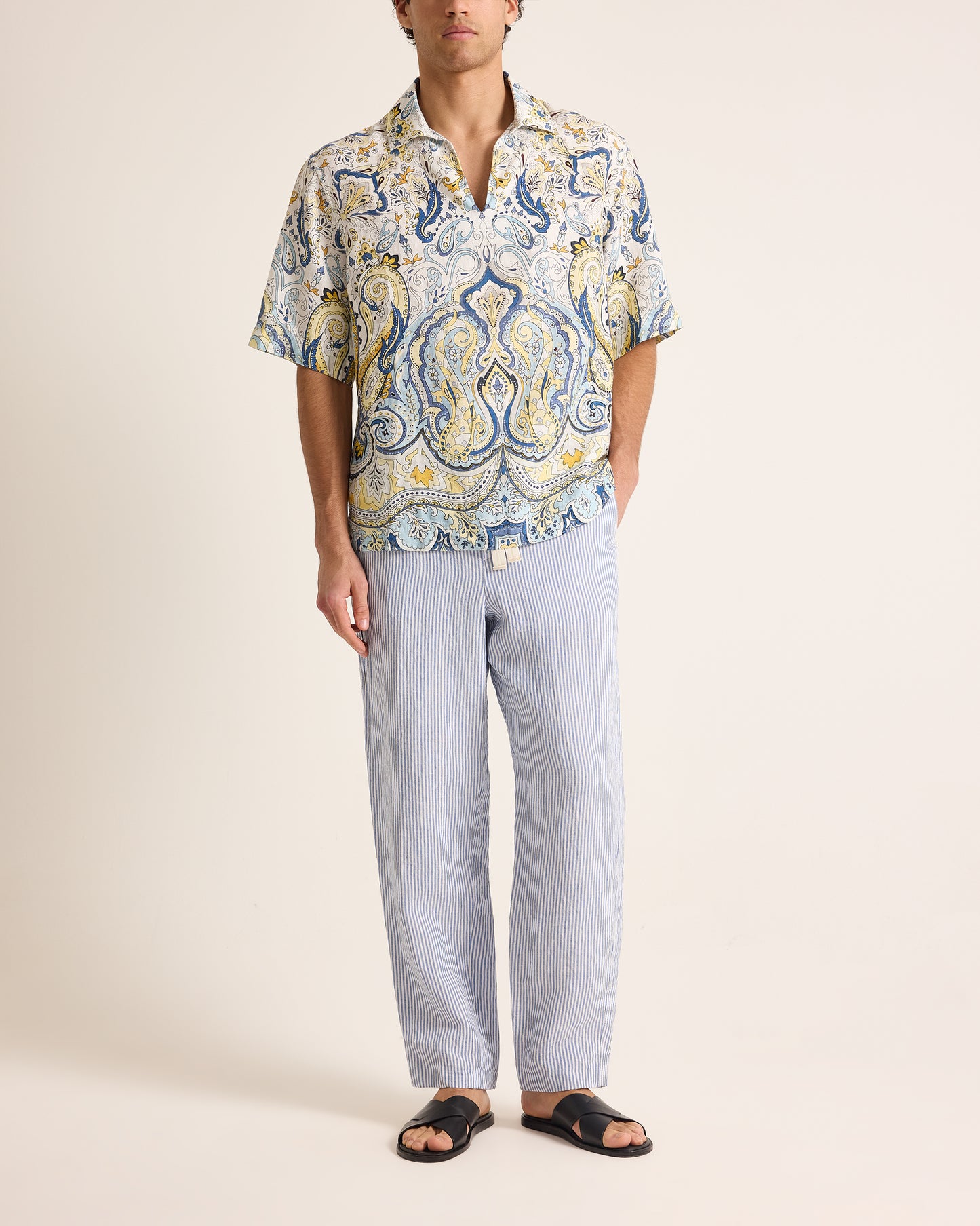 Man wearing a patterned shirt and light pants on a plain background