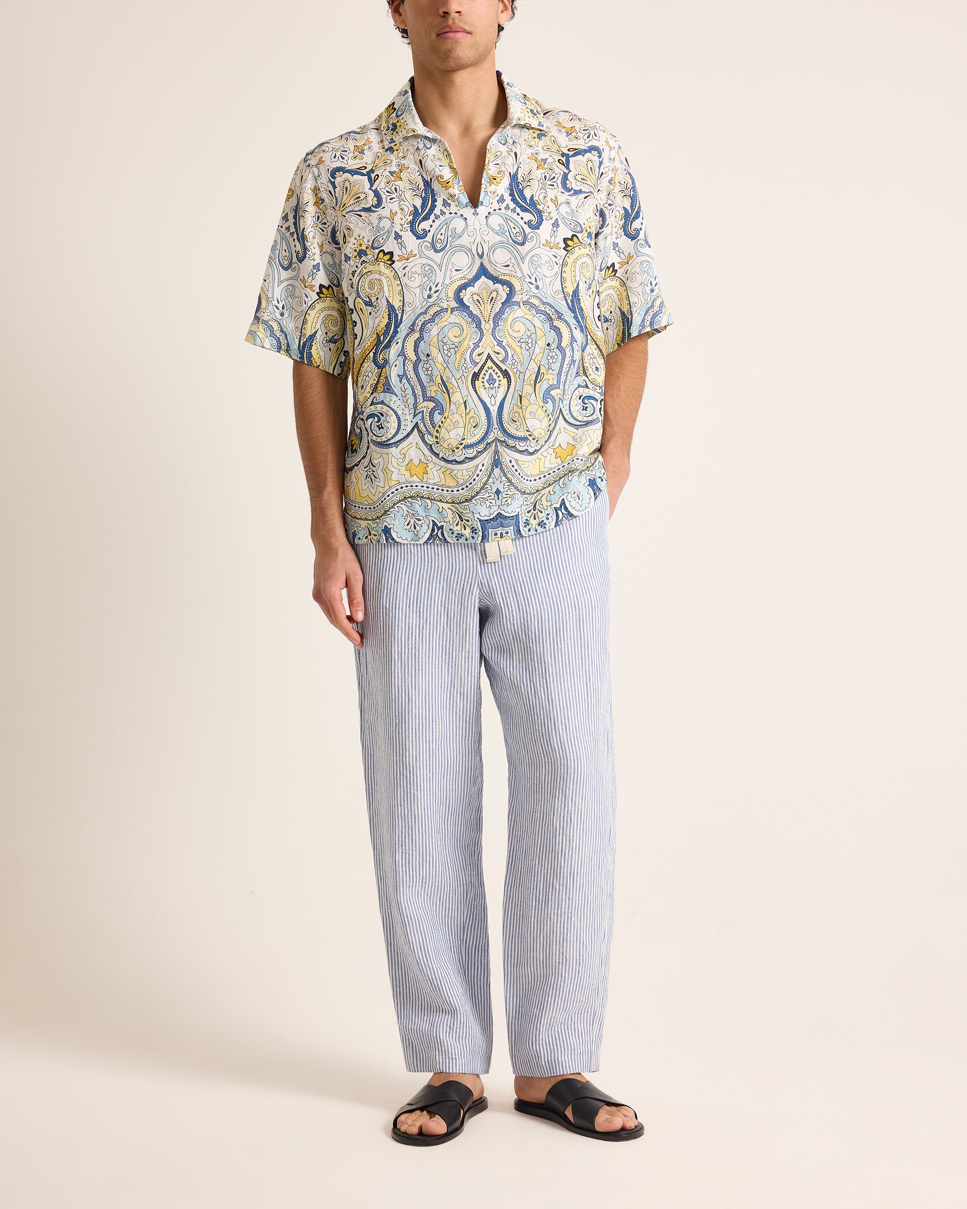 Man wearing a patterned shirt and light pants on a plain background