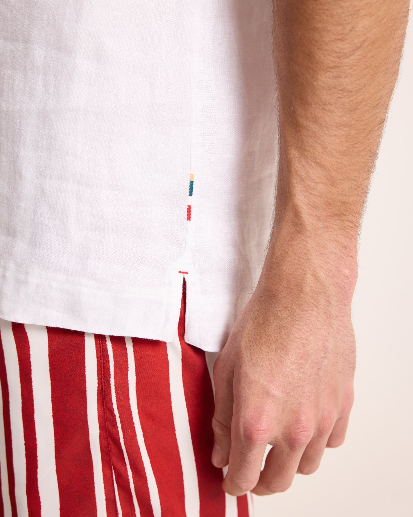 Close-up of a person wearing a white shirt with a small logo and red striped pants.