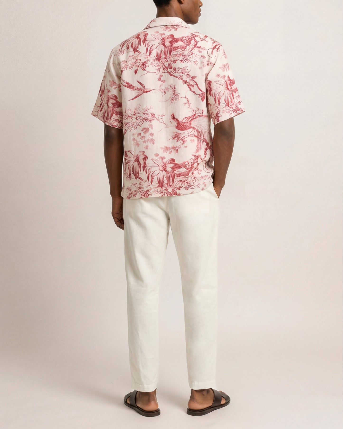Person wearing a red floral shirt and white pants on a plain background