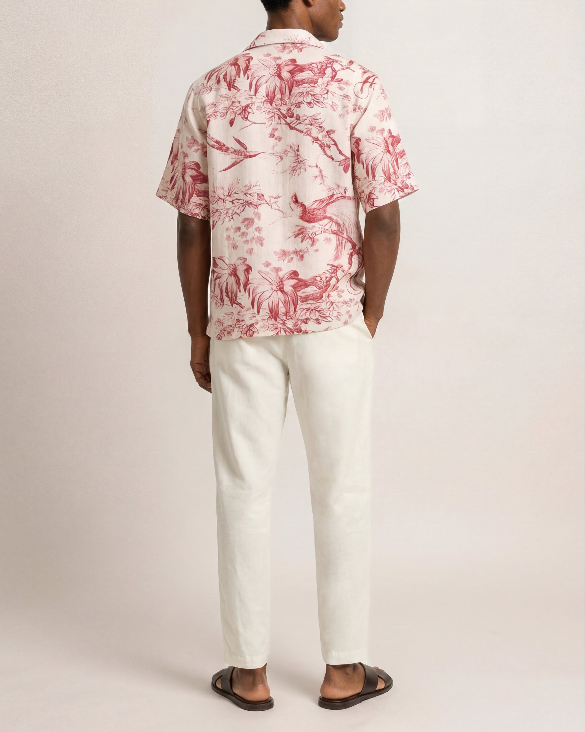 Person wearing a red floral shirt and white pants on a plain background
