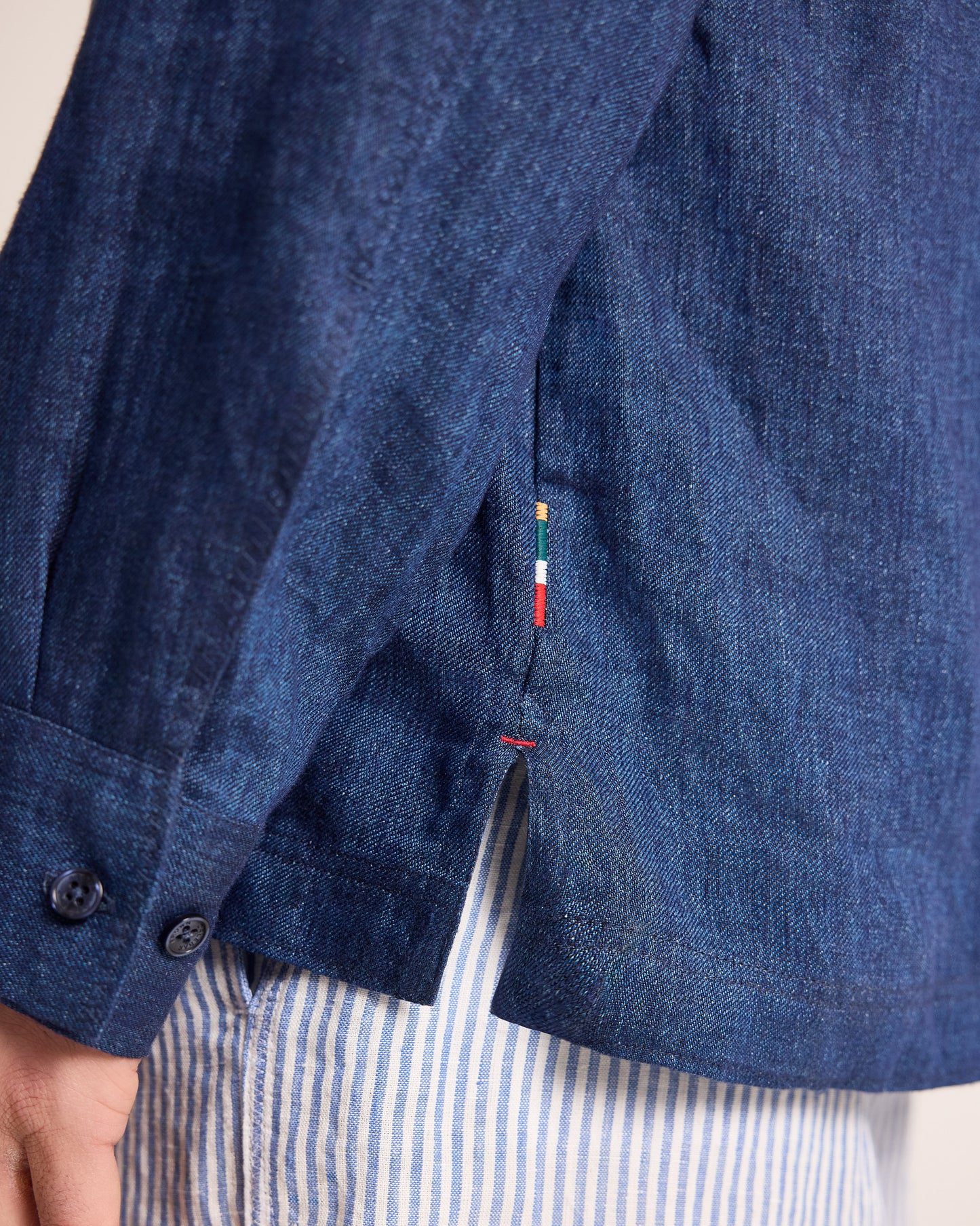 Close-up of a blue denim jacket with a brand tag, worn over a striped shirt.
