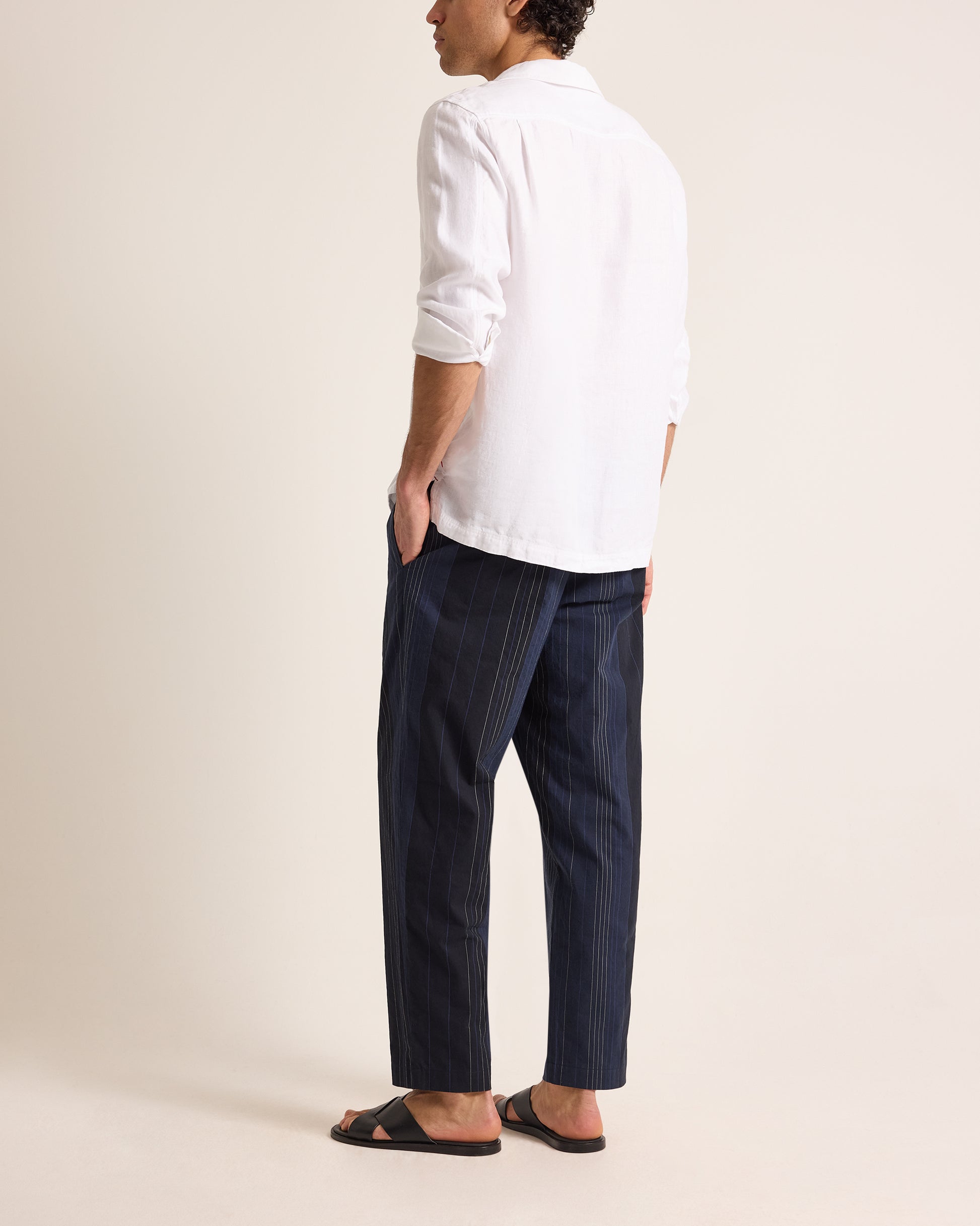 Person wearing a white shirt and dark striped pants on a beige background
