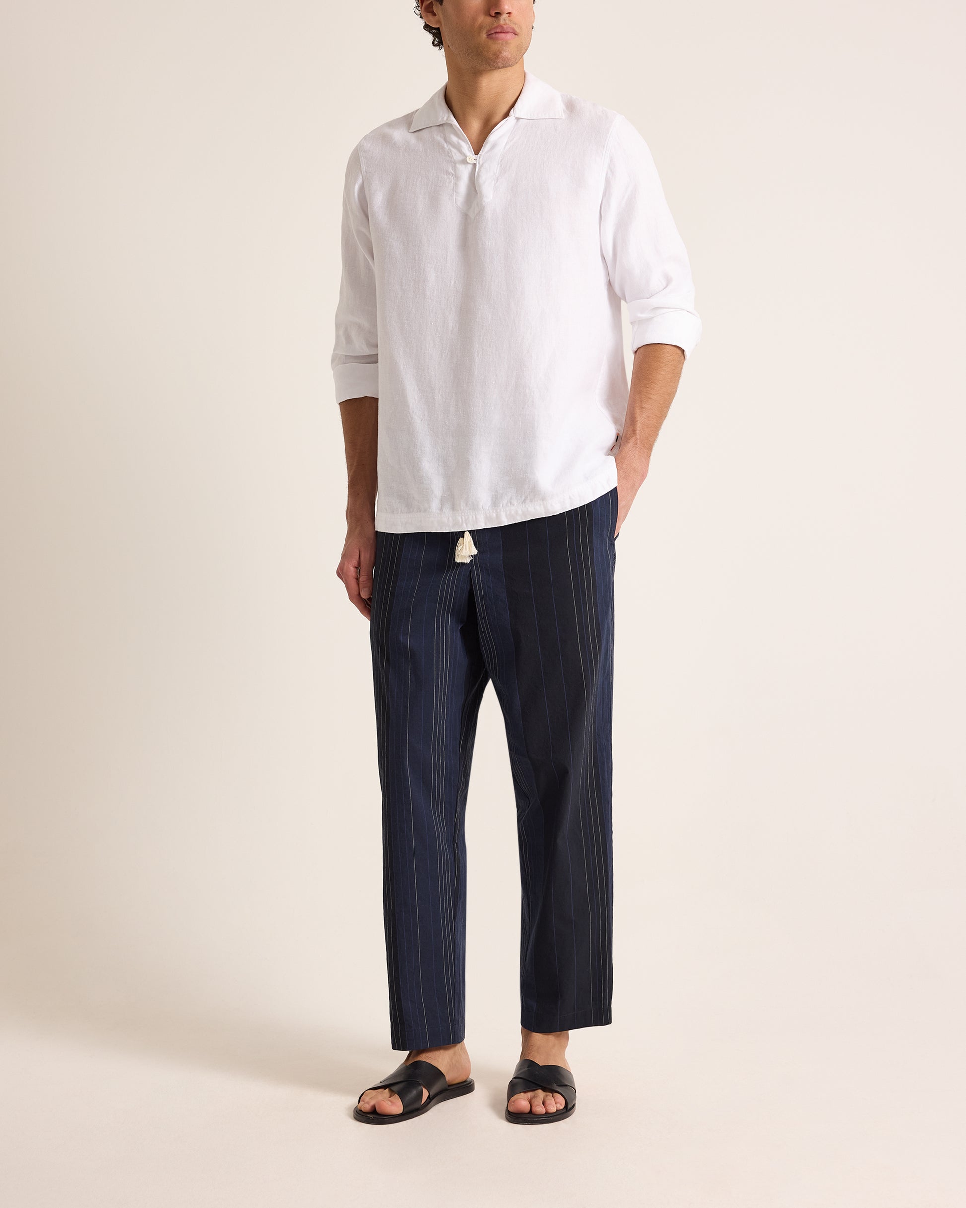 Person wearing a white shirt and dark striped pants on a beige background
