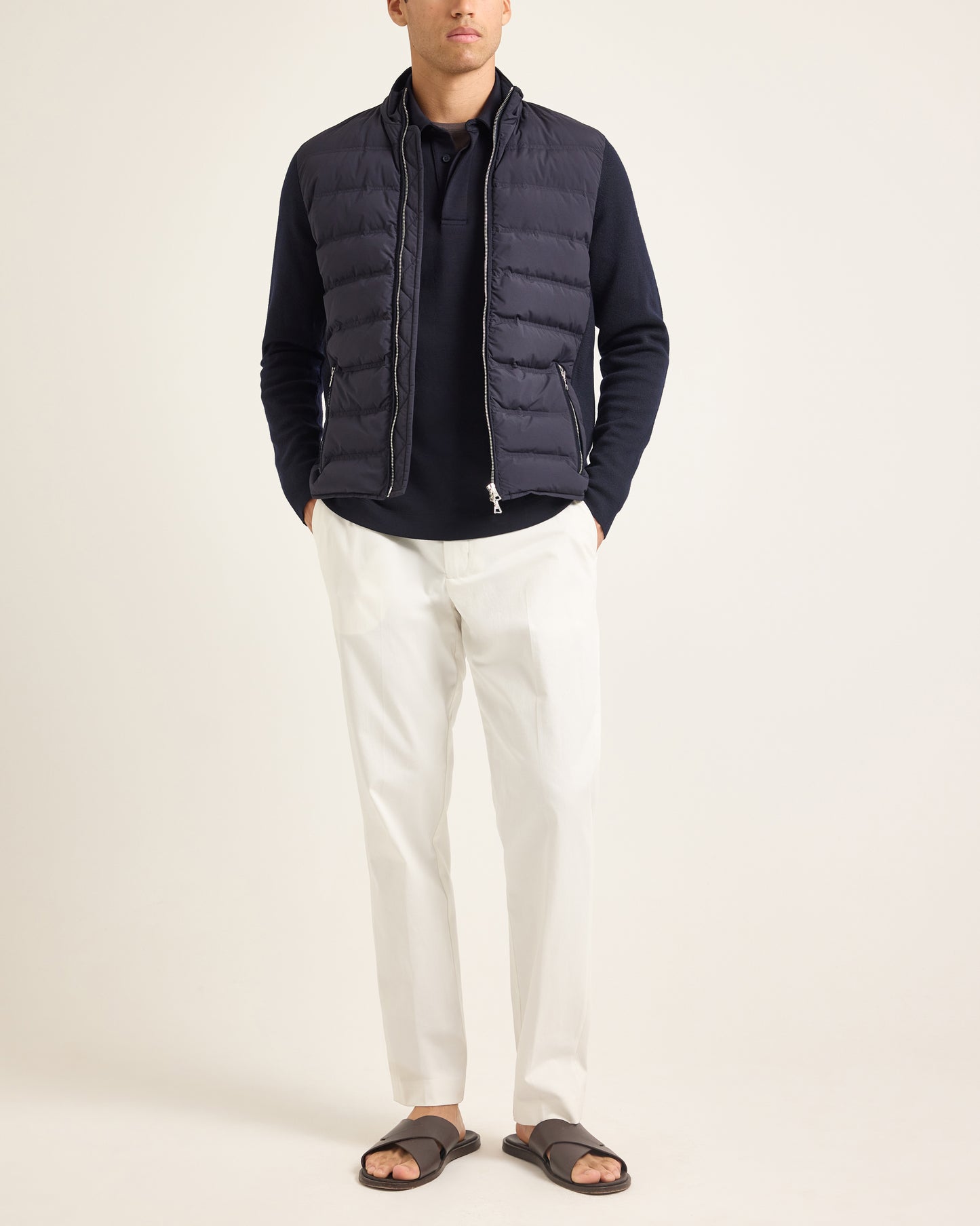 Model wearing navy padded jackets with navy polo shirt and white trousers on a plain background