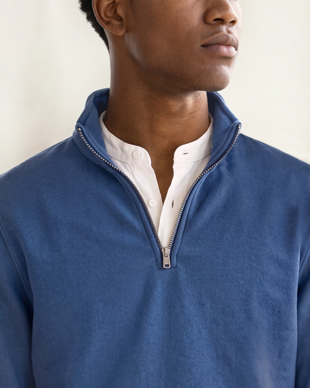Man wearing a dark blue quarter zip sweatshirt with white shirt underneath on a plain background