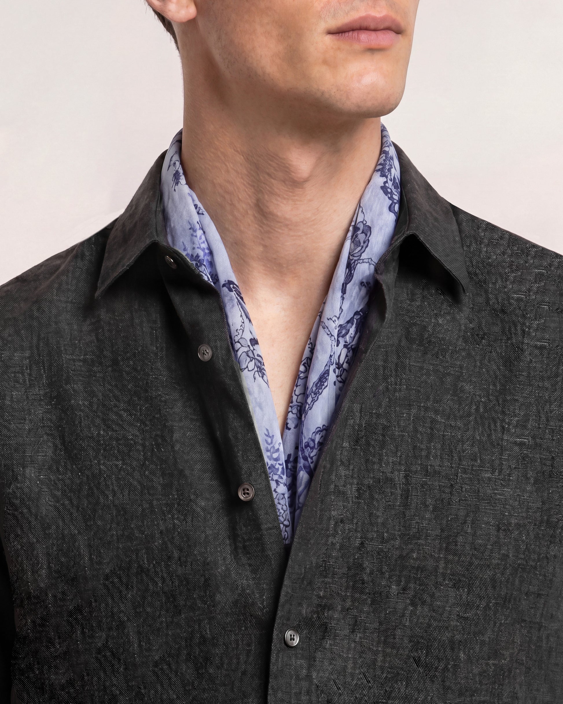 Man wearing a dark gray jacket over a light blue patterned shirt with a plain background