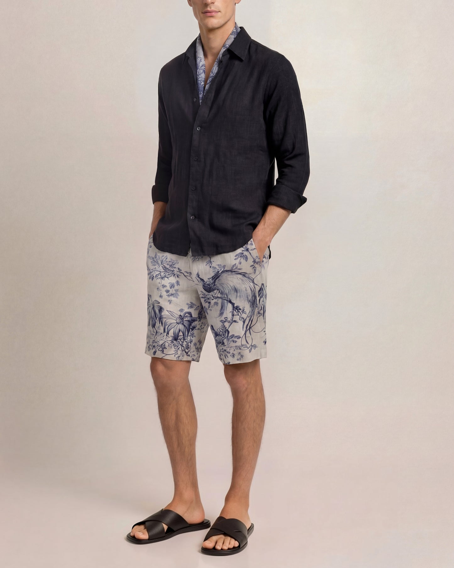 Man wearing a dark shirt and blue patterned shorts on a plain background
