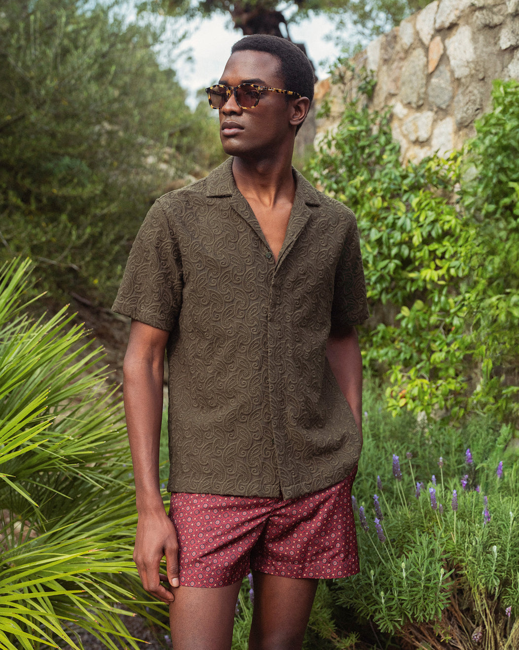 Man wearing a green shirt and red shorts standing in a garden.