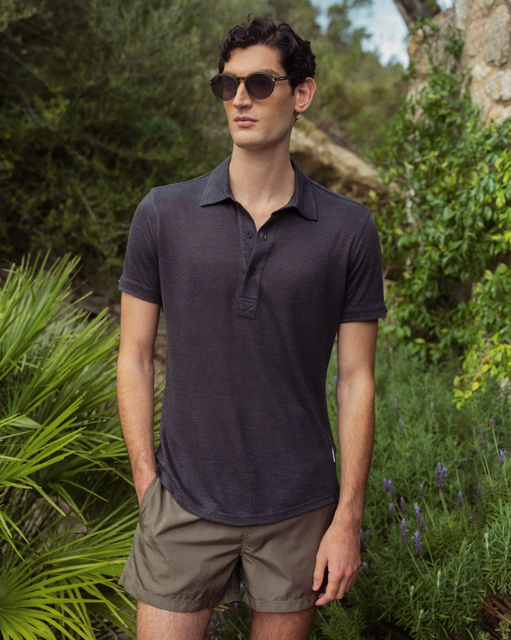 Man wearing a dark polo shirt and sunglasses outdoors with greenery in the background