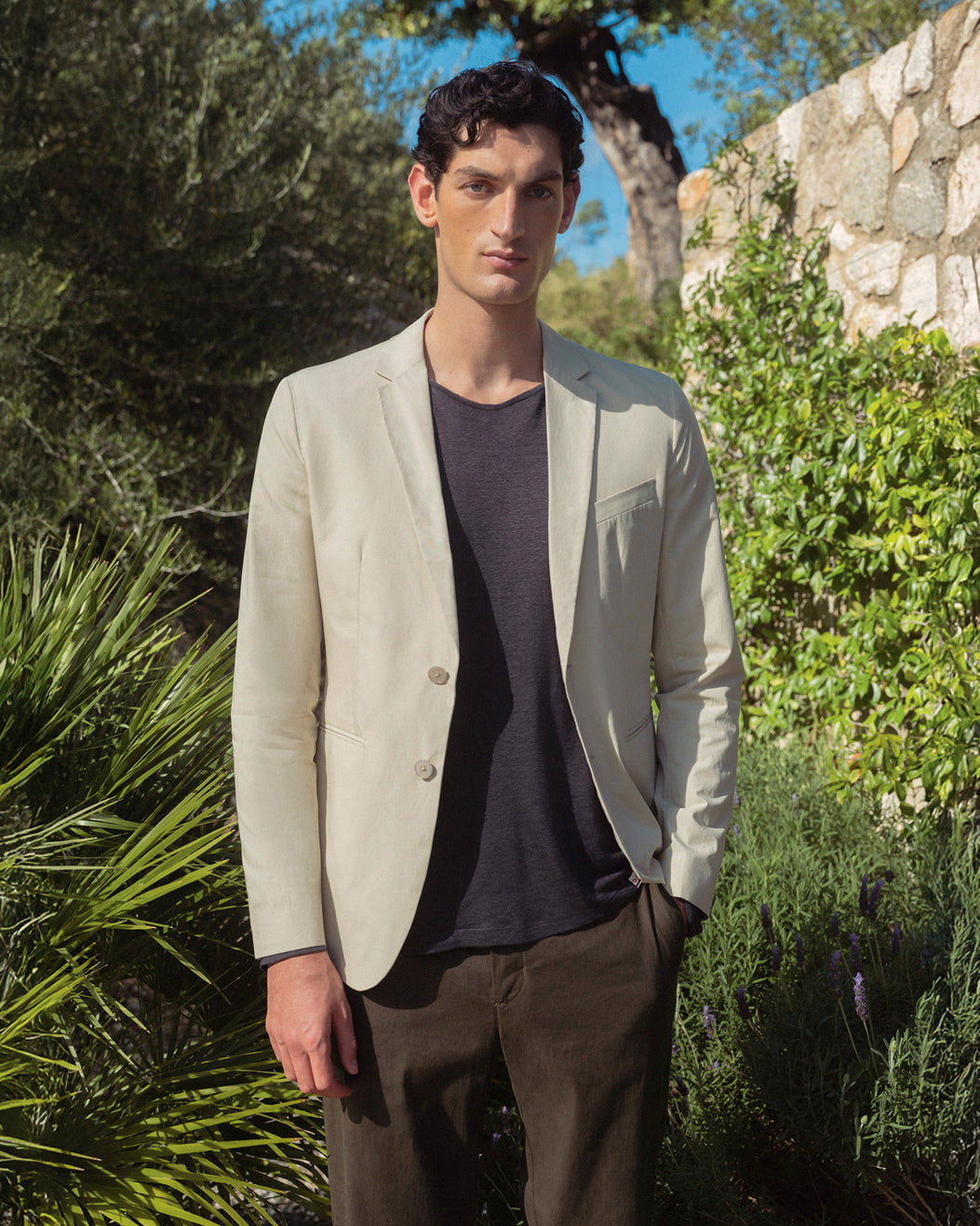 Man wearing a light beige blazer over a dark shirt in a garden setting