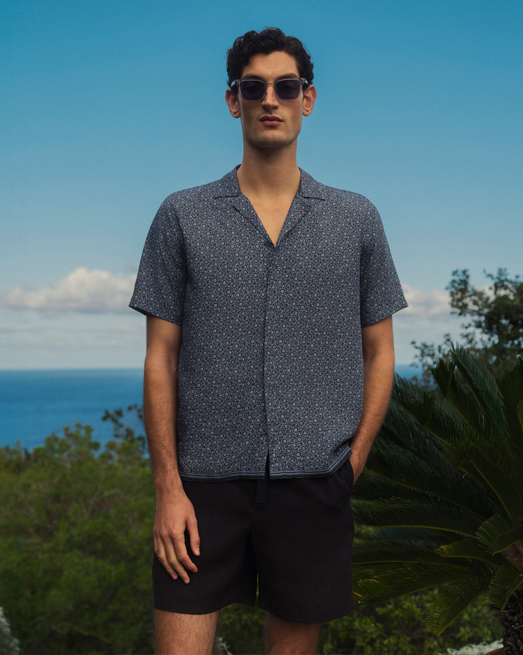 Man wearing a patterned shirt and sunglasses with a scenic background