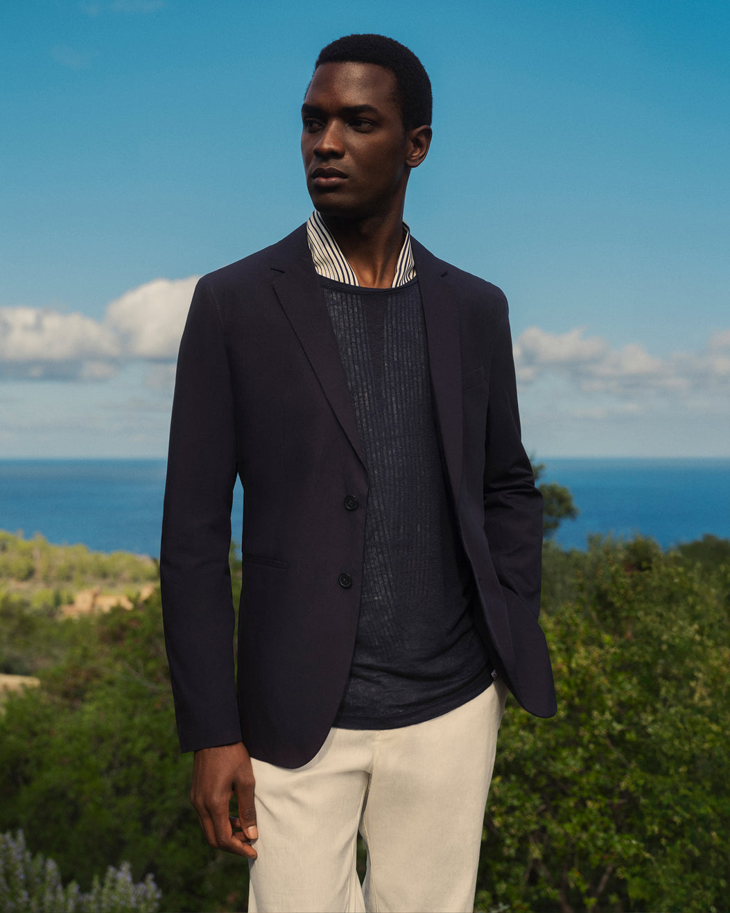 Man wearing a dark blazer over a striped shirt with a scenic background