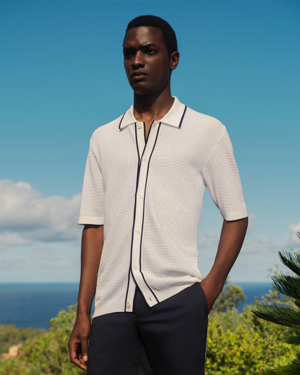 Man wearing a white patterned shirt with black accents outdoors against a blue sky.