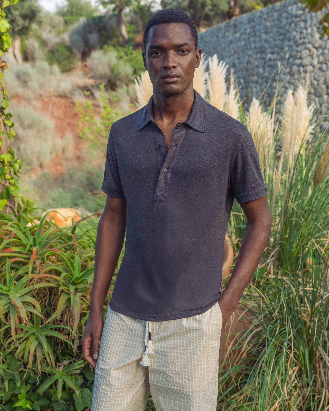 Man wearing a dark polo shirt standing in a garden with plants and rocks in the background
