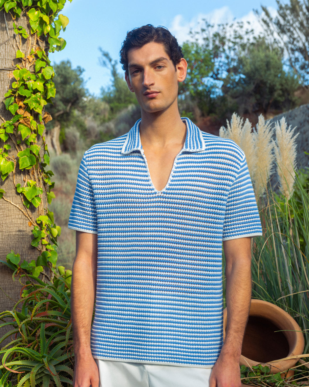 Man wearing blue and white striped crochet polo against greenery background
