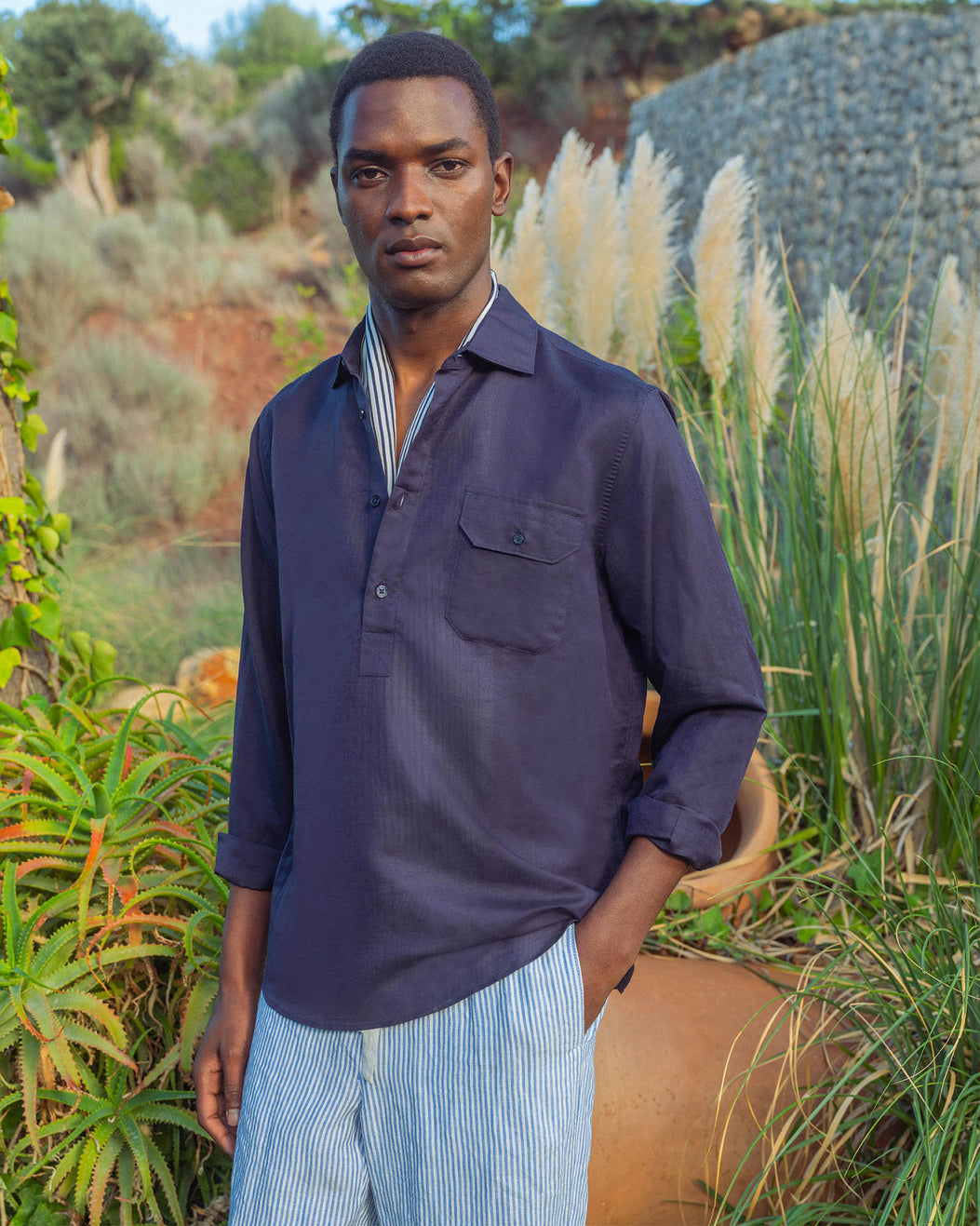 Man wearing a navy shirt and striped pants standing in a natural setting
