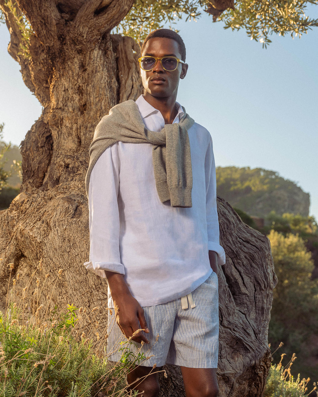 Man standing in a natural setting with a tree and mountains in the background