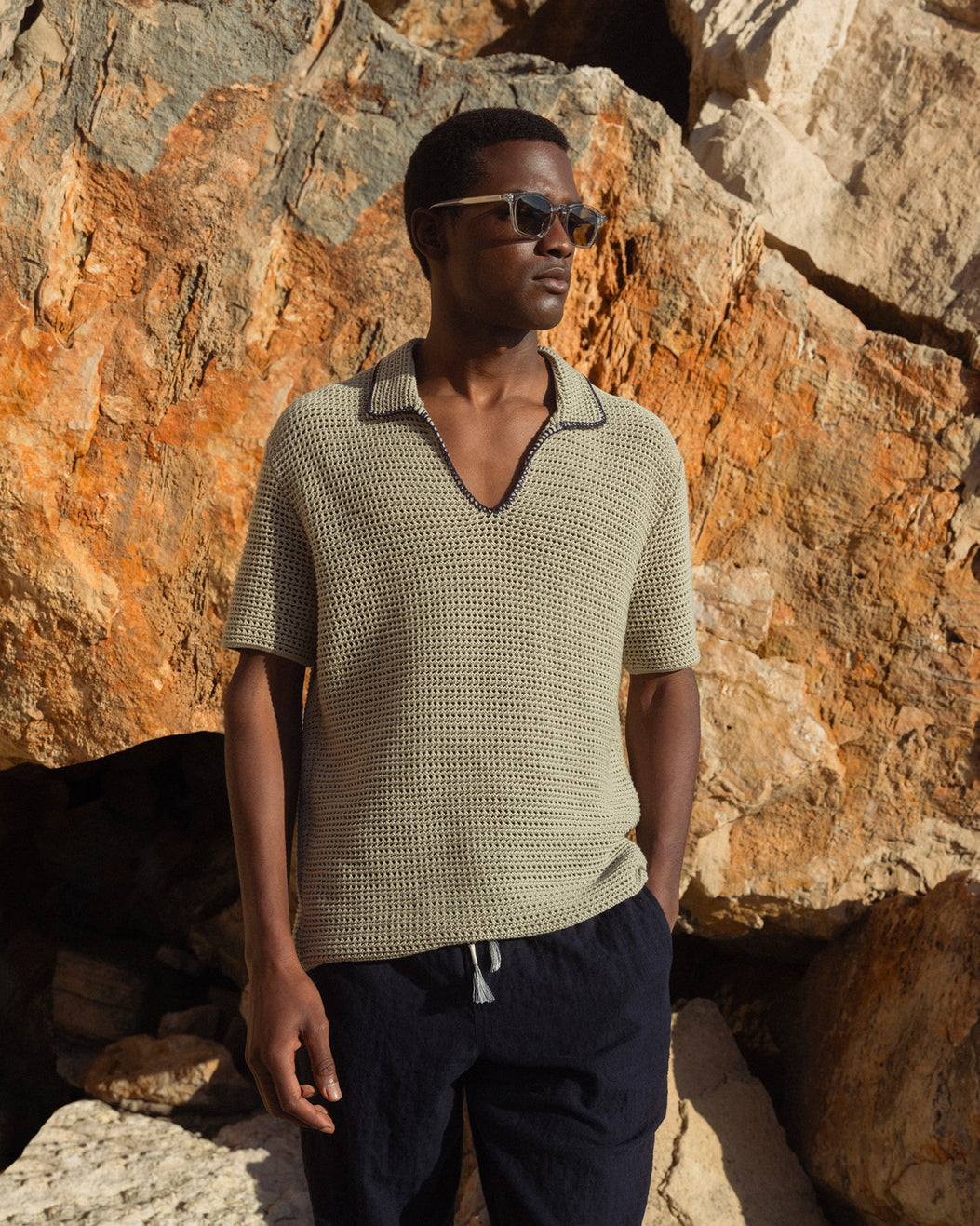 Man wearing a textured green shirt and sunglasses standing against a rocky background