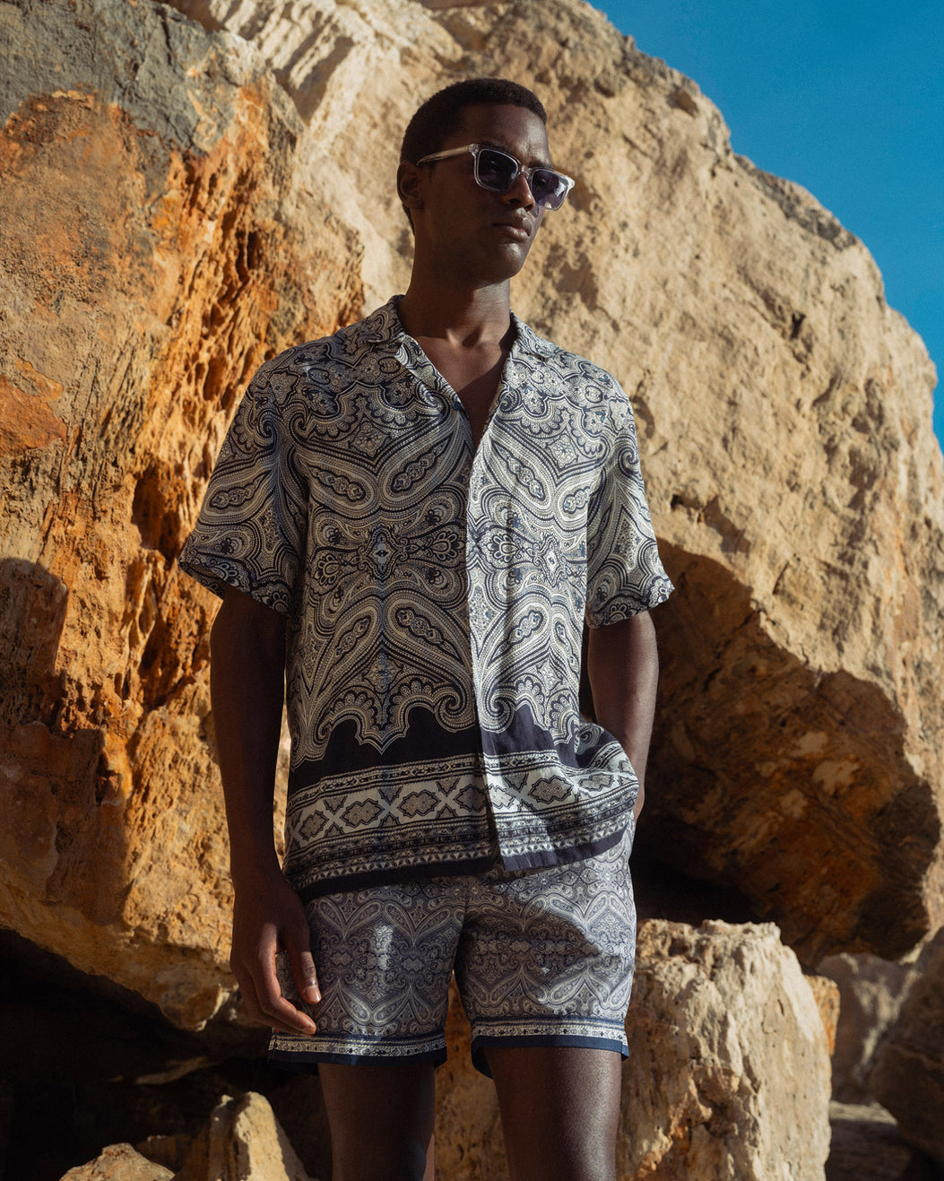 Man wearing a patterned outfit standing against rocky terrain