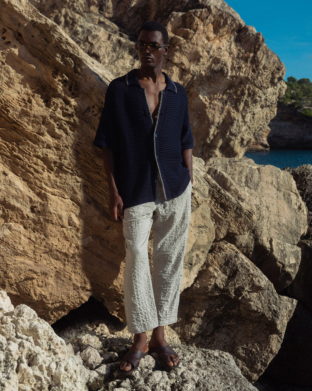 Man standing on rocky terrain wearing a dark shirt and light pants.