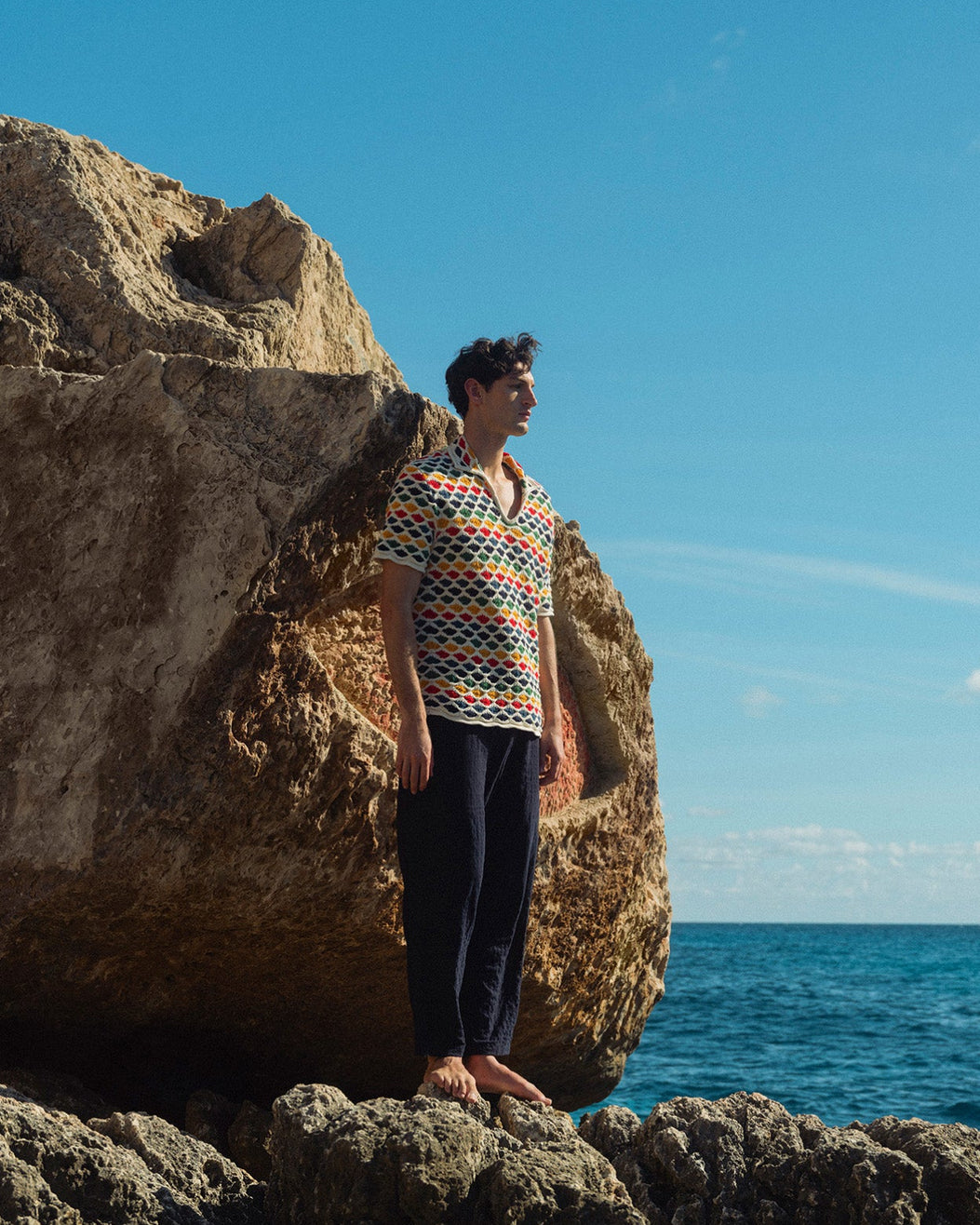 Person standing on a rocky outcrop by the ocean with a blue sky.