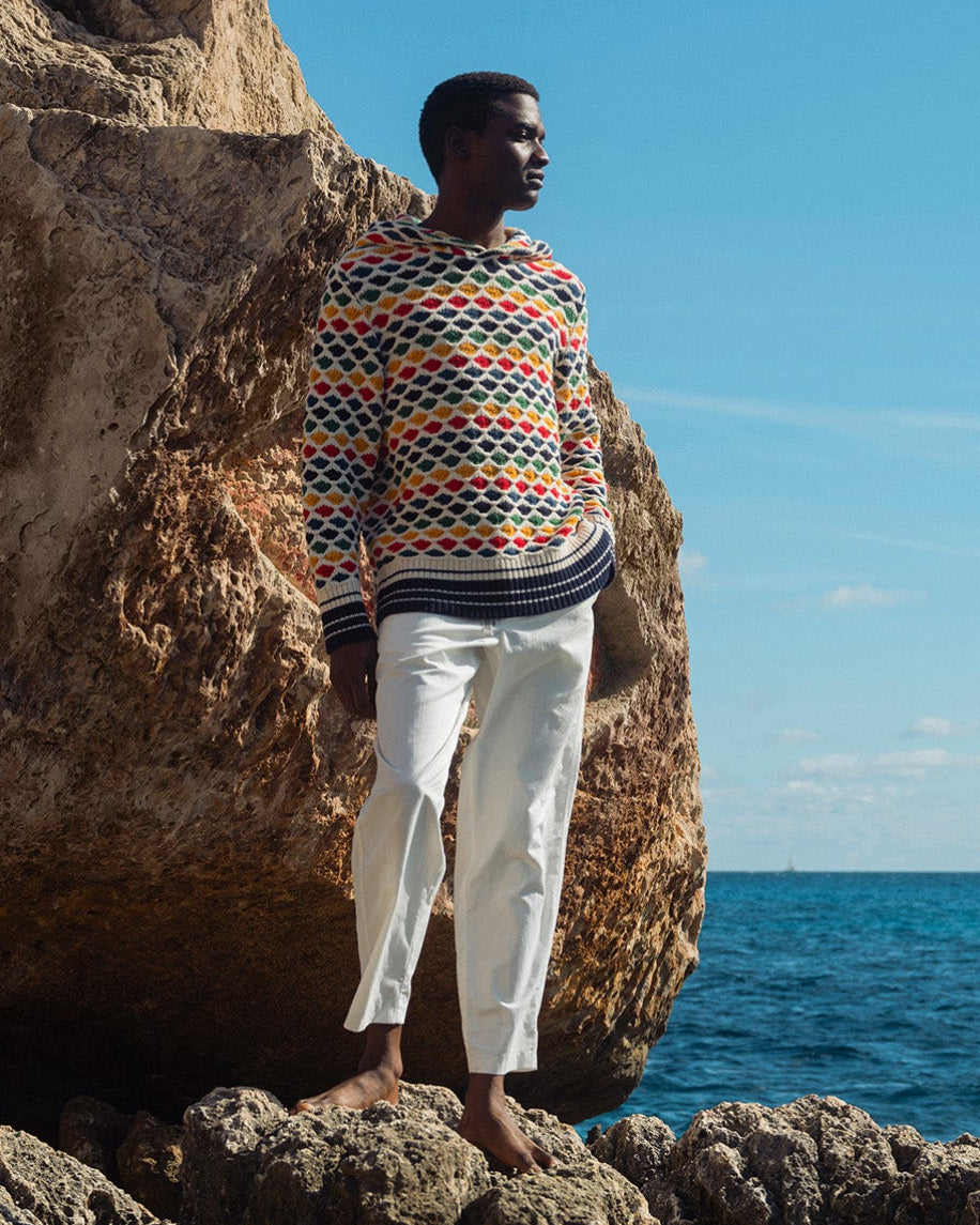 Person wearing a patterned sweater standing on rocks by the ocean