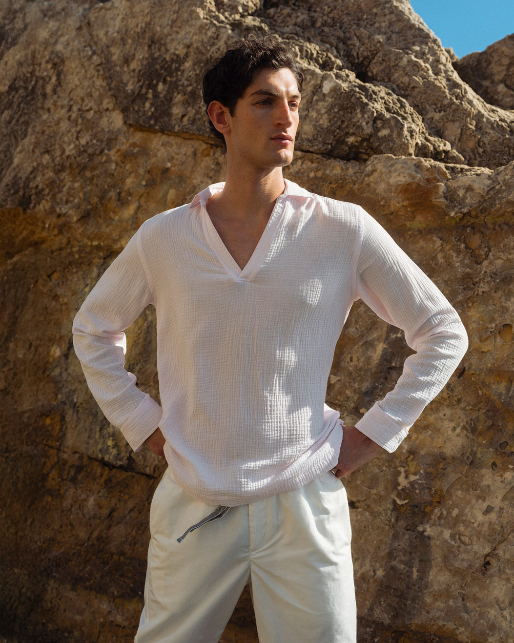 Man wearing a white shirt and pants standing against a rocky background