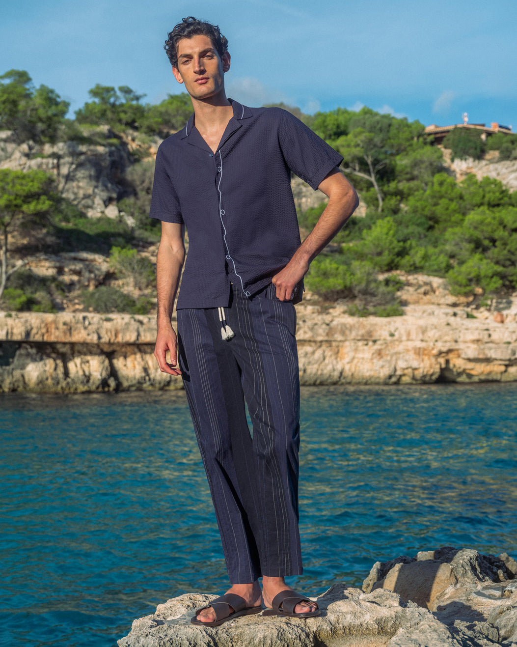 Man wearing navy shirt and trousers standing by the ocean