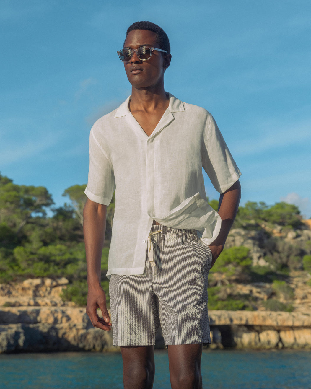 Man wearing sunglasses and a light-colored shirt with a scenic background