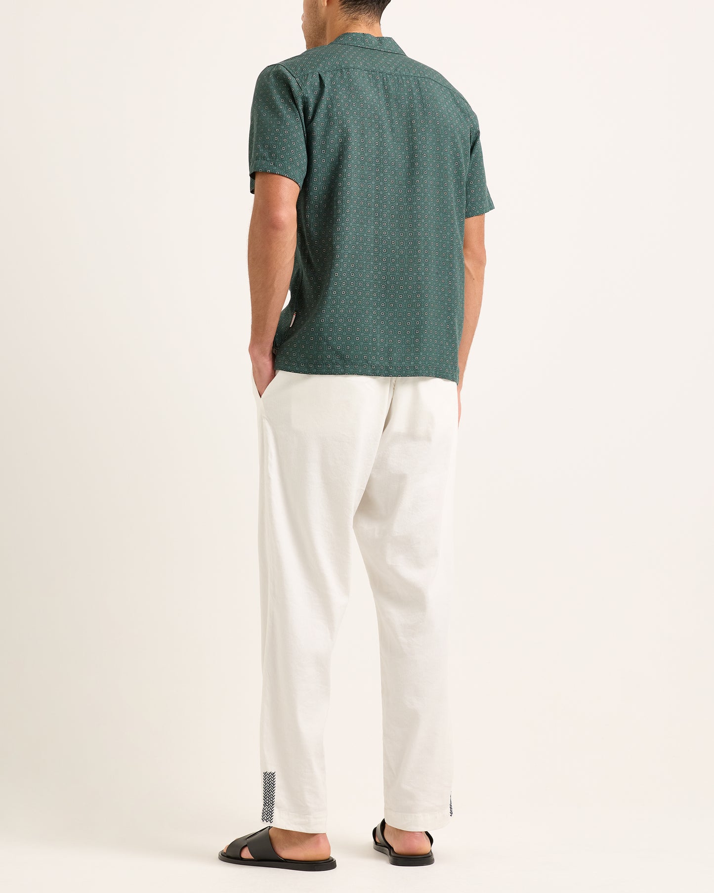 Model wearing dark green patterned short-sleeve shirt with white trousers on a white background