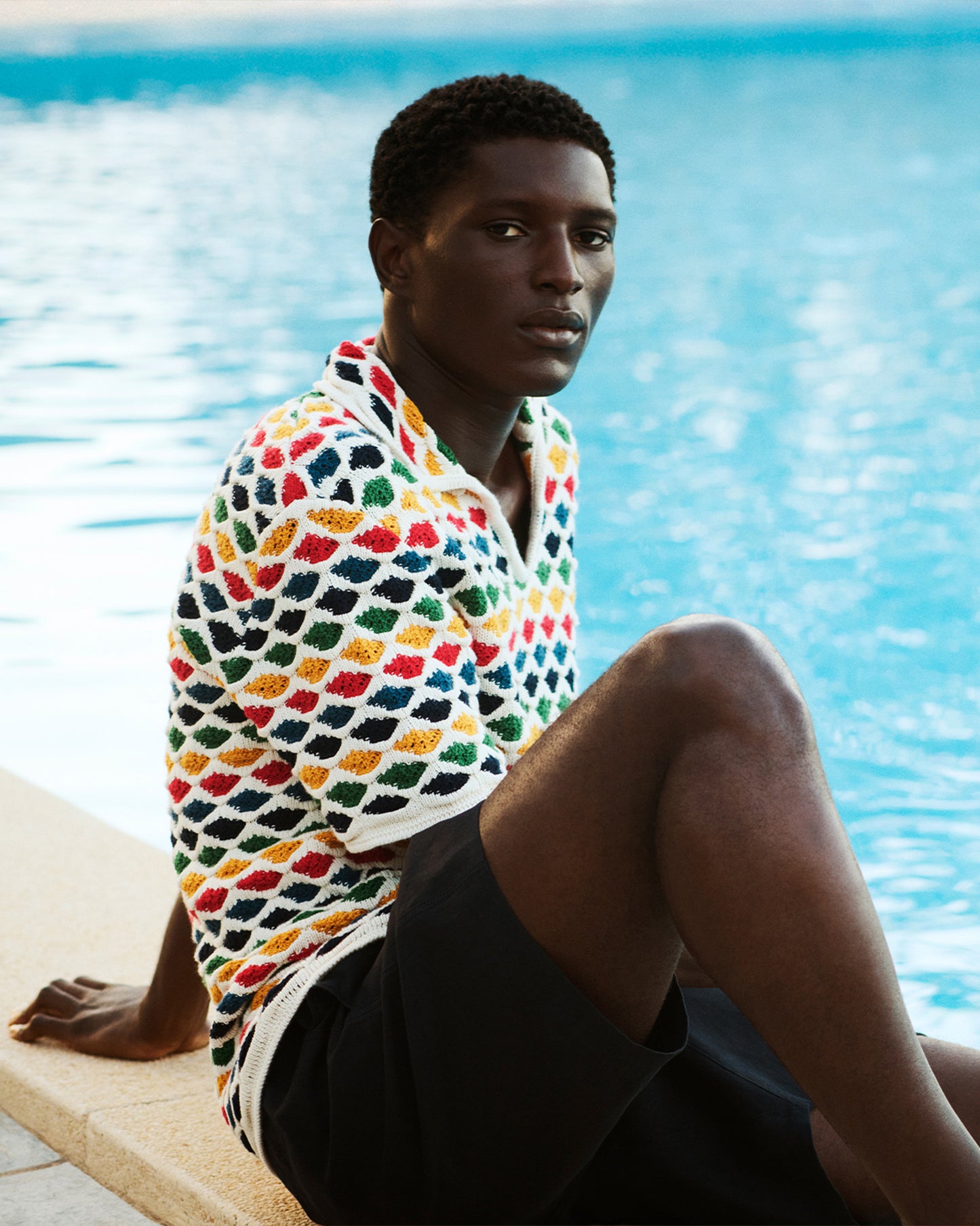 Person sitting by a pool wearing a colorful patterned polo shirt