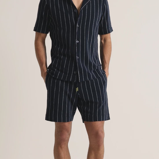 Man wearing striped navy towelling shirt and shorts on a plain background