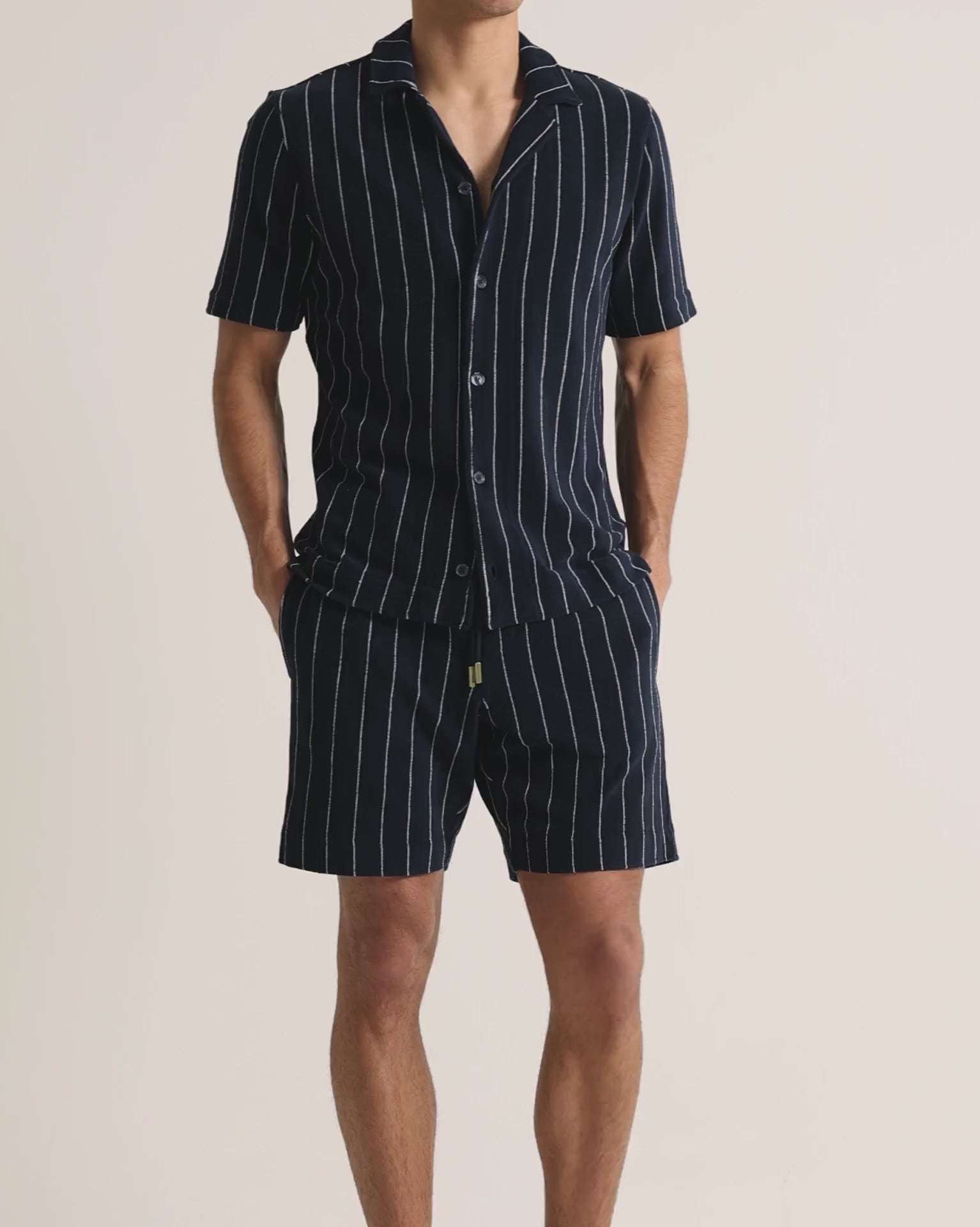 Man wearing striped navy towelling shirt and shorts on a plain background